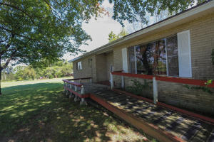 Home is located close to town, but has a country feel sitting atop 4 acres m/l with mature trees and a nice view. It has two living areas, two bedrooms, but the addition/enclosed garage with half-bath would make a great 3rd bedroom. Updated main bath with accessible shower. This home is comfortable and ready to move in, but could use a bit of TLC. Never have a water bill again if you don't want one! Its currently on well water, but can be reconnected to county water. Front porch under the shade trees has a great view, 2 ramps, attached two-car carport, detached metal shop/garage and a storage building!