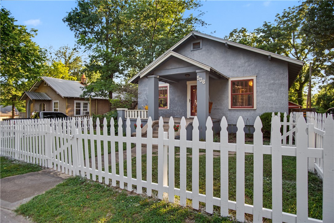 This inviting single-family residence offers approximately 1,090 sq ft of living space with 2 bedrooms and 1 bathroom on a nicely sized lot in an established neighborhood close to downtown amenities, parks, and local attractions. The exterior features classic gray/blue siding with white trim and a welcoming covered front porch. A white picket fence adds curb appeal and privacy, while mature trees shade the spacious backyard. A new roof (2025) will give you peace of mind. A detached red barn-style shed with power provides excellent storage or workshop space, and the backyard includes a wooden deck that was just finished being built, and fire pit area ideal for outdoor entertaining and relaxing evenings. Rear deck and elevated porch access further enhance the outdoor living opportunities. Inside, the open, light-filled layout includes hardwood-style flooring throughout much of the main living areas.