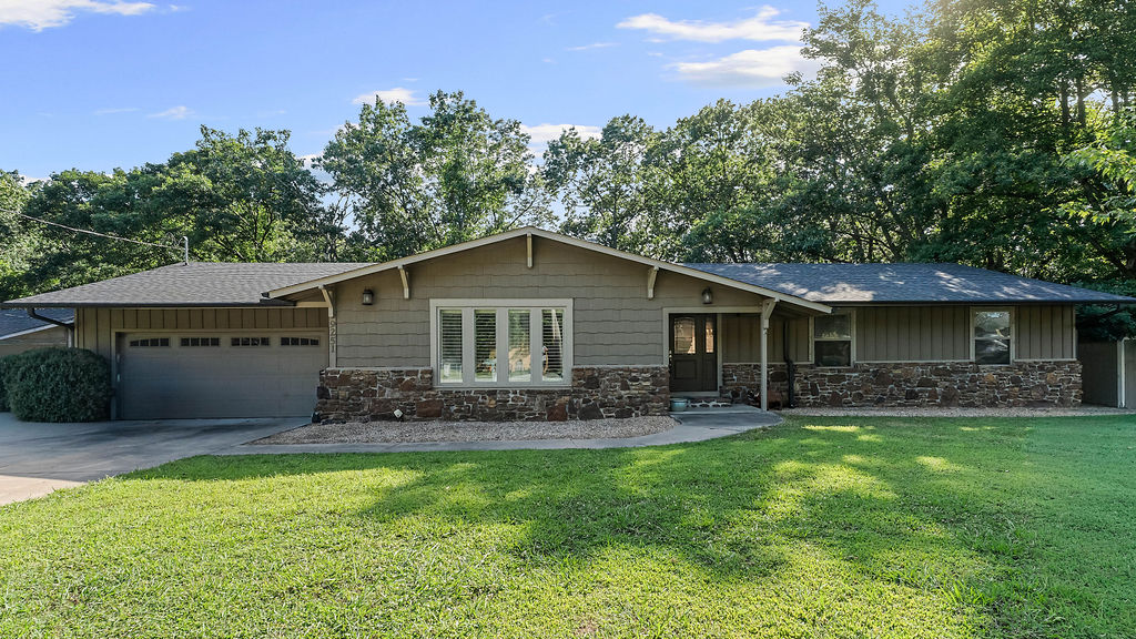 Don't judge this one by its cover — the outside is sweet and understated, but wait until you step inside. 9251 Grimes Drive is a lake-life dream tucked on a wooded third-acre lot near Prairie Creek Marina and Beaver Lake. Walk in and you're greeted by an open living room, formal dining, and an eat-in kitchen with quartz counters that feels straight out of a magazine. Wood and tile floors flow throughout, and downstairs the finished walk-out basement has a game room and wet bar made for hosting. Head outside to the covered patio and deck, wrapped in trees and total privacy. Boating, fishing, golf — it's all minutes away, and downtown Rogers' shops and restaurants are less than 5 miles out. Weekend getaway or full-time home, this one's the whole package hiding behind a modest exterior.