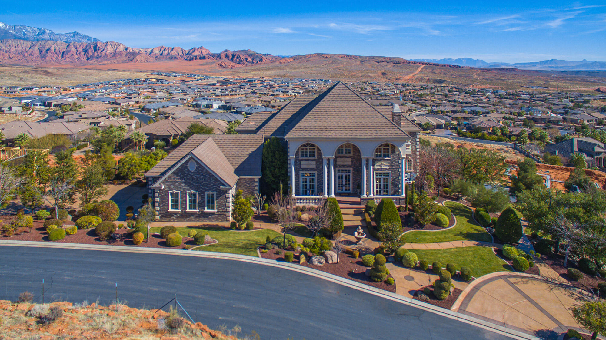 This timeless brick estate home is enveloped with mature, park-like landscaping yet also located at the top of Green Springs capturing expansive views from Pine Valley to Zion National Park.
Exceptional craftsmanship is showcased throughout, including a grand foyer with a curved staircase, detailed millwork, and a striking two-story heirloom library wrapped in rich wood moldings.
Utilize kitchens on both the primary and secondary levels for entertaining, along with formal living and dining rooms. Enjoy a home theater, game room, and dedicated home gym. The elevator adds everyday convenience and long-term flexibility. An oversized five-car garage provides ample space for vehicles, storage, and hobbies. This home offers a serene setting for recreation and relaxation.