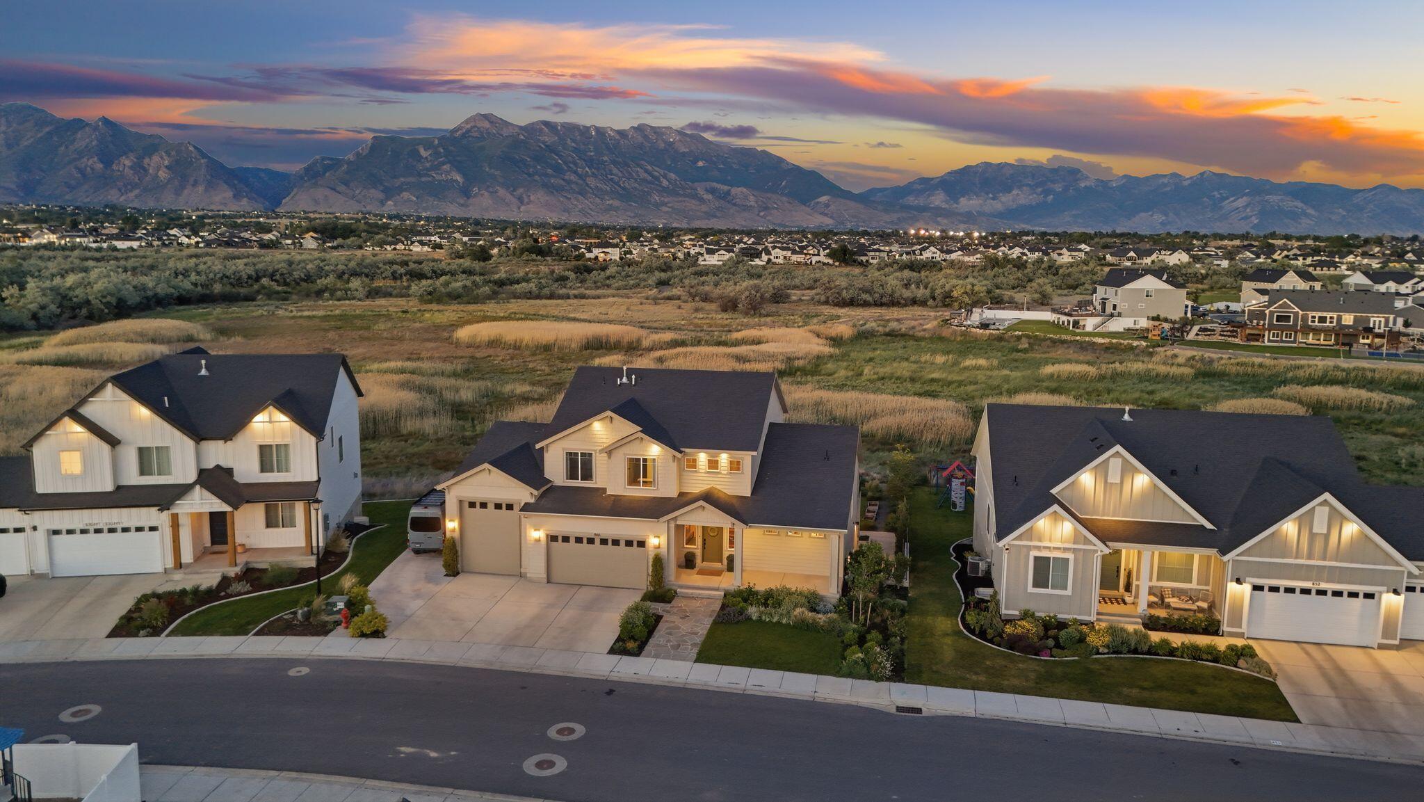 Experience exceptional privacy, breathtaking mountain views, and an unmatched lifestyle in the heart of Silicon Slopes. Backing to protected wetlands with no rear neighbors, this professionally designed residence offers a rare combination of open space, natural beauty, and refined living. Inspired by Architectural Digest, the home features soaring ceilings, expansive picture windows, and thoughtfully curated interiors that seamlessly blend modern design with warmth and functionality. The stunning chef's kitchen serves as the heart of the home, showcasing a massive quartz island, custom cabinetry, designer lighting, double ovens, open shelving, and effortless flow into the surrounding living and dining spaces. Walls of glass frame unobstructed Wasatch Mountain views and flood the home with natural light. The dramatic great room features two-story ceilings, a statement fireplace, and oversized windows that bring the outdoors in. Multiple gathering spaces throughout the home provide exceptional flexibility for entertaining, including a spacious lower-level family room, dedicated theater room, home gym, and a beautifully designed music room with custom coffered ceiling details and panoramic views. Outdoor living is equally impressive. The backyard is a private retreat designed for wellness and recreation, complete with a private pump track, sauna, outdoor shower, cold plunge, and an expansive 60-foot deck ideal for entertaining or simply enjoying the peaceful surroundings. Covered outdoor living space below the deck creates year-round enjoyment while preserving the incredible mountain backdrop. Additional highlights include an oversized RV garage, a remarkable walk-in closet with its own washer and dryer, dual-zone HVAC, a 9.6 kW solar system, EV charger, and a 220V outlet in the garage. Ideally located just minutes from I-15, Silicon Slopes, top-rated schools, dining, and shopping, with world-class skiing and outdoor recreation within easy reach.