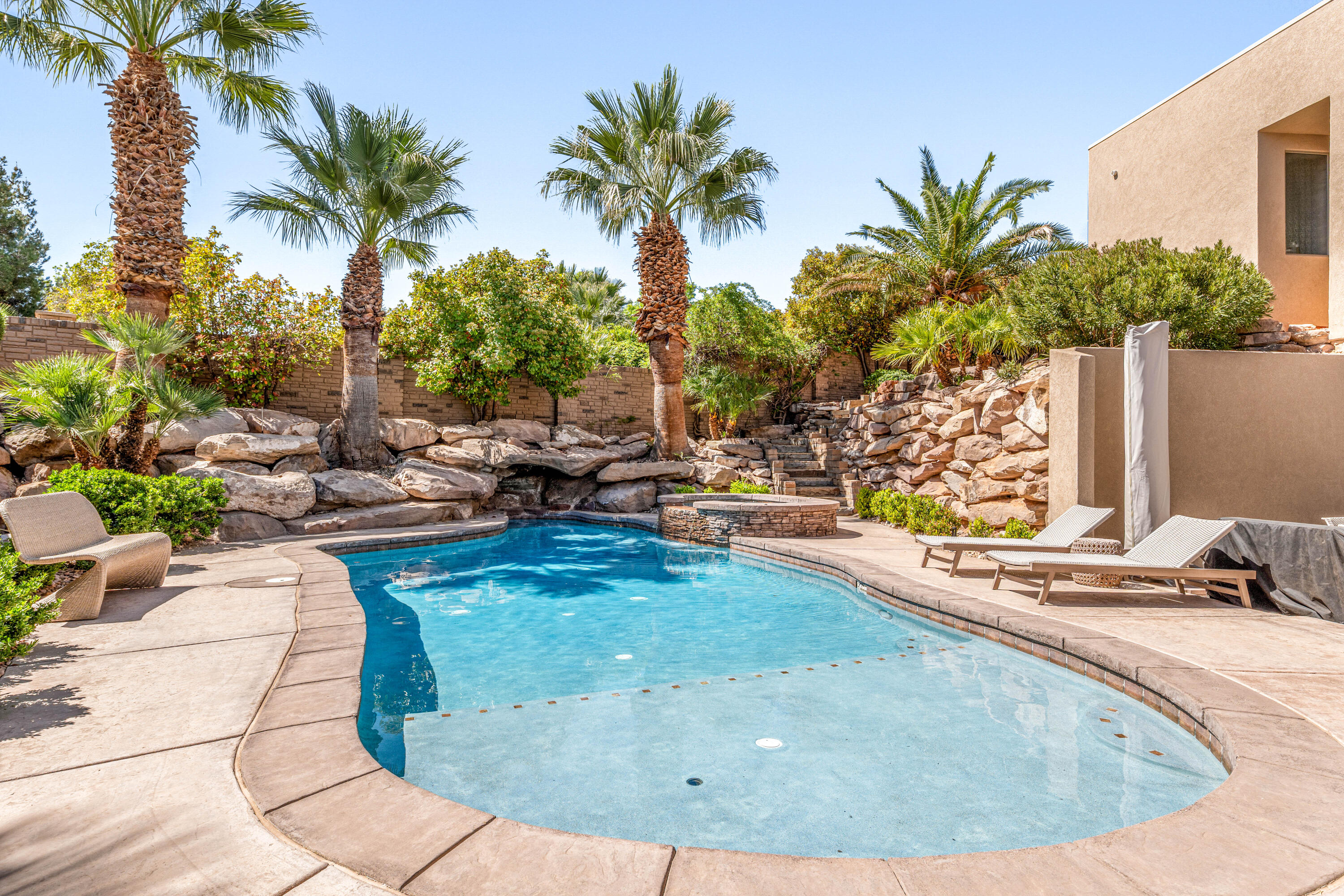 Tucked within the gated community of Stone Cliff, this residence offers timeless design and effortless livability--set against some of St. George's most iconic red rock views. Grounded in natural materials and classic finishes, the home carries a sense of quiet elegance and warmth. Thoughtfully scaled spaces are filled with natural light, and the surrounding desert landscape feels present in nearly every room--framed, not just glimpsed. The main level is made for gathering. Multiple patios extend off the kitchen for seamless indoor-outdoor living, while a canopy of mature trees creates the kind of shaded backyard that's equally at home hosting a dinner party or a holiday card photoshoot. The primary suite functions as a true retreat--complete with a sitting area where you can unwind with a book or simply take in the elevated views over the pool and landscape below. Downstairs, the walkout level opens directly to the saltwater pool--finished with a sun shelf, spa, and water feature. The space is flexible enough for recreation, hosting guests, or multi-generational living, and a dedicated poolside room adds the kind of practical convenience that makes everyday life easier. A craft room sits adjacent to the laundry, and a workshop connects to the fourth garage--room for hobbies, projects, or whatever you've been meaning to get to. Sellers would PREFER to offer home turnkey with furnishings included, this move-in-ready home works equally well as a primary residence or a second-home retreat.
Stone Cliff is one of St. George's most sought-after communities--private, well appointed amenities, and close to the outdoor recreation that defines life here.