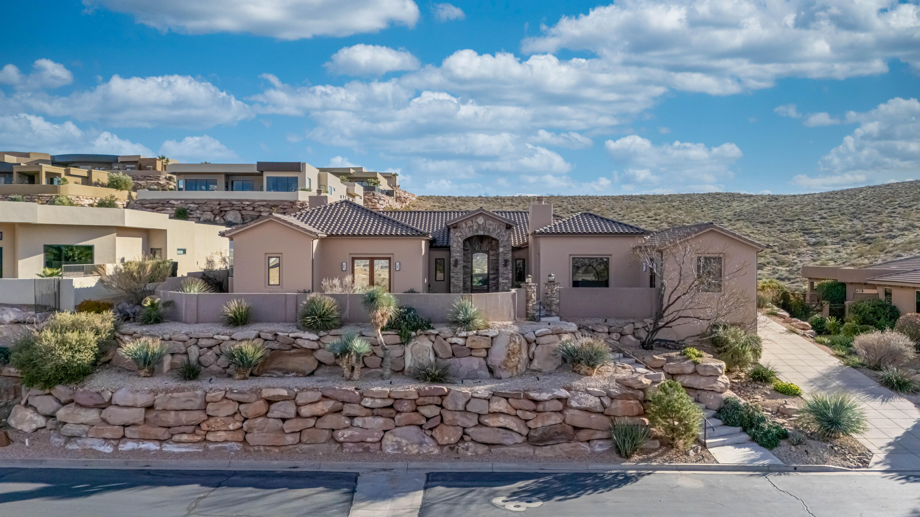 Perched high in the gated community of Stonecliff, this 5,488 square foot Tuscan inspired retreat captures sweeping views of Pine Valley Mountain & all of Washington County from the front courtyard. The views continue from the primary suite, home office, & private casita bedroom, creating a daily reminder of why you live in Southern Utah. With 5 bedrooms, 4 bathrooms, multiple laundry areas, and a sprawling kitchen featuring multiple ovens, sinks, & refrigerators, this custom home was built for hosting & everyday living. Interior stone accents add warmth and texture, while the covered patio & NO backyard neighbors provide privacy that is hard to find. Residents enjoy Stonecliff amenities including a clubhouse, fitness center, tennis courts, pickleball courts, & a resort style pools! Beyond the main living spaces, this property continues to separate itself through its setting and layout. Elevated above much of the city, the home captures layered views that shift throughout the day. Snow dusted Pine Valley Mountain in the winter. Deep red cliffs glowing at sunset. City lights flickering below at night. The perspective from this lot gives you both distance and connection at the same time.

Large windows were positioned to frame those views from key rooms, including the primary suite and office, so the scenery becomes part of everyday life rather than something you only notice from the patio. Even interior hallways feel intentional, drawing your eye outward.

The backyard borders open space, which means no direct rear neighbors and a buffer that is difficult to replicate. The covered patio is generous in size and functions as a true extension of the home. It is set up for outdoor dining, quiet mornings, or evenings spent watching storms roll across the valley.

Living in Stonecliff also means access to community amenities that support an active lifestyle. Residents enjoy a private clubhouse, fitness center, tennis courts, pickleball courts, and a pool and spa that rival many resorts. The gated entrance adds a layer of privacy, while the elevated location keeps you just minutes from dining, shopping, golf, and medical services.

Properties that combine scale, privacy, and panoramic views within a gated setting are limited. This home offers all three in one of St. George's most established communities.