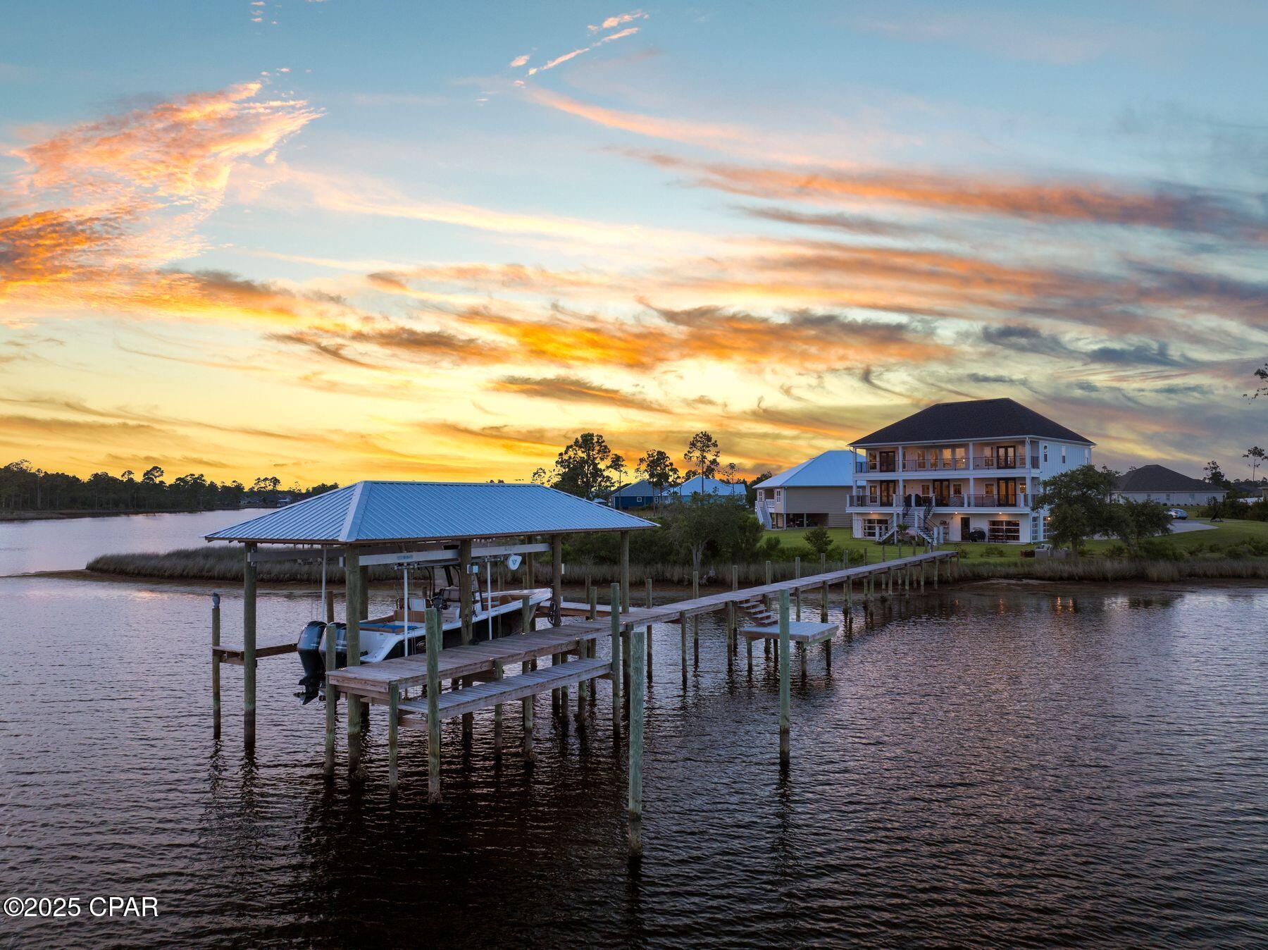 This custom-built waterfront retreat is more than a home; it's a private resort with panoramic bay views, a boat lift with rare DEEP WATER ACCESS, and a show stopping game room unlike anything else. Presiding over North Bay, this home offers expansive living and soaring ceilings. This luxurious residence enjoys a quiet location set back from the street at the end of a cul-de-sac. Built in 2021, the home offers a magnificent game room/den complete with an island bar, dining area, pool table, and space for a home gym, tabletop games, and indoor ball sports. Multiple TVs provide the ultimate viewing for sports fans. Garage-style glass doors fully open to allow refreshing breezes indoors when dining on this level. As you approach the home, a broad staircase leads up to the main level. LVP flooring flows seamlessly through the open living space, formal dining area, and a spacious sitting room. Every seat has stunning views across the bay. A soaring volume ceiling with clerestory windows enhances the space and brings in an abundance of natural light. Gather around the gas fireplace after dinner and enjoy quality time with family and friends. The tall chimney wrapped in shiplap is the focal point of the living room. Lit by three pendant lights, the generous island announces the chef's kitchen, which is equipped with KitchenAid appliances, including a double oven. A pot filler is conveniently located above the smooth top range, ready for pasta nights. A walk-in pantry, laundry, and a wine bar make this the perfect home for entertaining. A wall of windows delivers sweeping bay views, which only get better when you step through the French doors onto the large covered composite deck. From the porch a staircase leads down to the manicured backyard. The primary suite is also on this floor and boasts a boutique-sized walk-in closet and beautiful bay views. The ensuite bathroom impresses with shiplap walls, a dual quartz-topped vanity, and a walk in shower wrapped with tile and glass. A neat makeup area completes this private haven. A guest bedroom, suitable for use as an office, and additional full bath completes the main level. Connected by a galleried walkway, the top floor comprises five additional bedrooms and two full bathrooms, as well as a bonus room. Doors open directly onto another full-width covered porch showing off the best views of the property. Where better to sip cocktails while toasting the sunset over the bay? The home features a two-car garage on the main level and an additional one and a half car garage on the lower level. A community pool offers more recreation beyond boating, fishing, kayaking, and paddle boarding from your private dock.