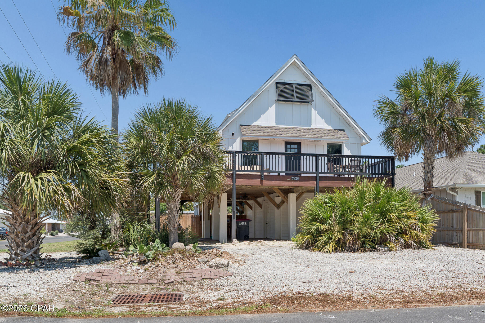Turnkey and ready. Welcome to Dolphin Den -- a fully furnished 3BR/3BA coastal showpiece in the heart of Biltmore Beach, three blocks to sugar-white sand and 226 feet to the Dolphin Drive boat ramp. From the moment you arrive, the home's crisp white board-and-batten exterior, classic gabled roofline, and elevated wraparound deck capture the timeless Florida beach-cottage charm buyers dream about. Peek between the swaying palms and you'll catch glimpses of the bay just beyond -- your daily view from sunrise coffee to sunset cocktails.
The expansive elevated deck is the heart of outdoor living here: an alfresco dining set for four, a separate lounge area with cushioned seating, a grill ready for fresh catch, and room to entertain a crowd under the Gulf Coast sky. Inside: a main-floor king primary suite with double vanities and walk-in shower, an upstairs queen retreat, and a bunk room built for the kids. Open-concept living flows out to those bay views through every window. Stainless kitchen, smart TVs in every bedroom, 58'' living room screen, and a game room with two stand-up arcades.
Outside, mature palms and tropical landscaping frame a fully fenced corner lot with parking for four plus your boat, jet ski, or golf cart. Elevated construction means no flood insurance required -- along with no HOA, a 2020 roof, HVAC, and water heater, and a termite bond in place. The lower level beneath the home is plumbed and wired, ready to expand your square footage and your vision. Whether you're after a primary residence, a second home, or a proven short-term rental in one of PCB's most walkable beach neighborhoods -- Dolphin Den is the rare property that checks every box. Don't just buy a home. Buy the lifestyle.