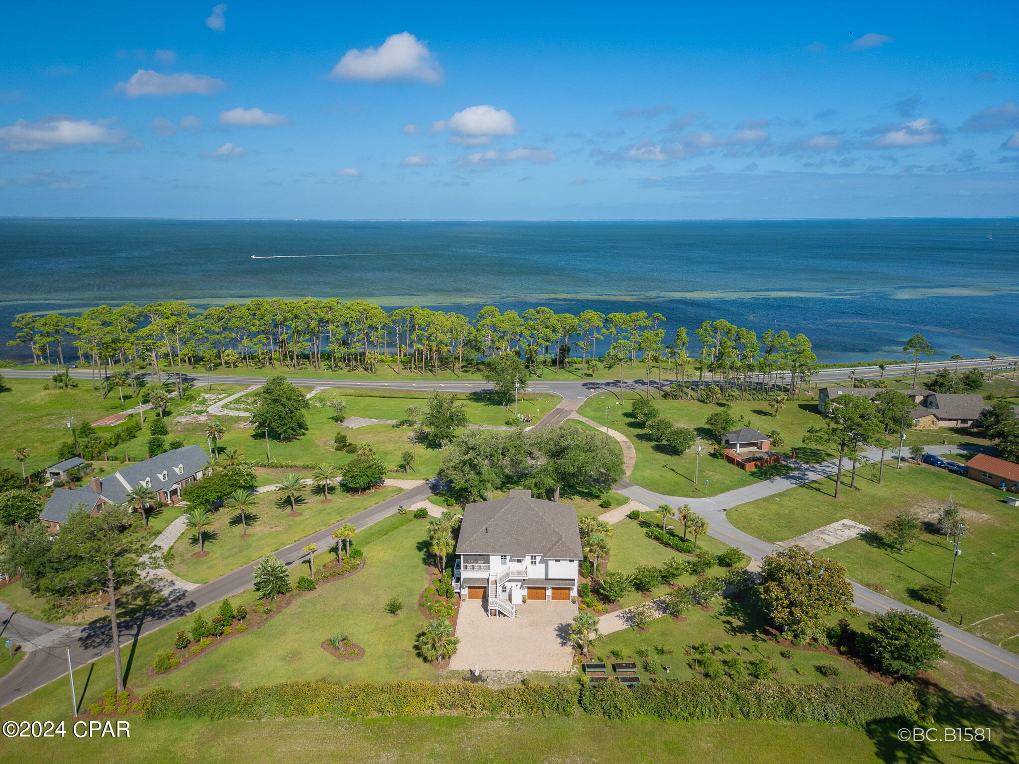 A rare 2020 Windolf-built estate on a .91-acre double lot inside the city of Port St. Joe, with panoramic views of St. Joseph Bay from every principal room. The kind of home that does not become available -- engineered for permanence and built to be passed down. Constructed to last generations: reinforced concrete foundation, full block-and-Hardie exterior, foam insulation between every interior room, hurricane-rated impact windows, standing-seam metal roof, whole-house generator, tankless water heater, natural gas, irrigation well, and underground utilities. Inside, craftsmanship reads immediately. Ten-foot ceilings, mahogany double-door entry, wide-plank Carolina Pine COREtec and hardwood floors, plantation shutters, and custom millwork throughout. The chef's kitchen features fully custom cabinetry, professional gas range with vent hood, wine refrigerator, oversized island, and walk-in pantry. A gas fireplace and built-in bookcases anchor the living room beneath French doors framing the bay. Formal dining and wet bar extend the entertaining footprint. The primary suite is a private retreat with sitting area, two walk-in closets, spa bath with garden tub, separate tile shower, double vanities, and screened porch access. A full elevator serves all three levels, and the home was designed for full wheelchair accessibility, including ADA-compliant baths, without compromising elegance. Three additional bedrooms, a bunk room, game lounge, and workshop provide flexible room for guests and hobbies. Wraparound covered and screened porches run the full length of the home. Mature live oaks, magnolias, palms, and fruit trees frame a circular drive to a three-car attached garage. RV sewer hookup, outdoor shower, and a prepared outdoor kitchen site are in place. Nearly an acre of level, walkable land -- a near impossibility inside city limits -- minutes from downtown, the marina, and Cape San Blas. Most furnishings negotiable. 3D Matterport tour available. Showings by appointment.