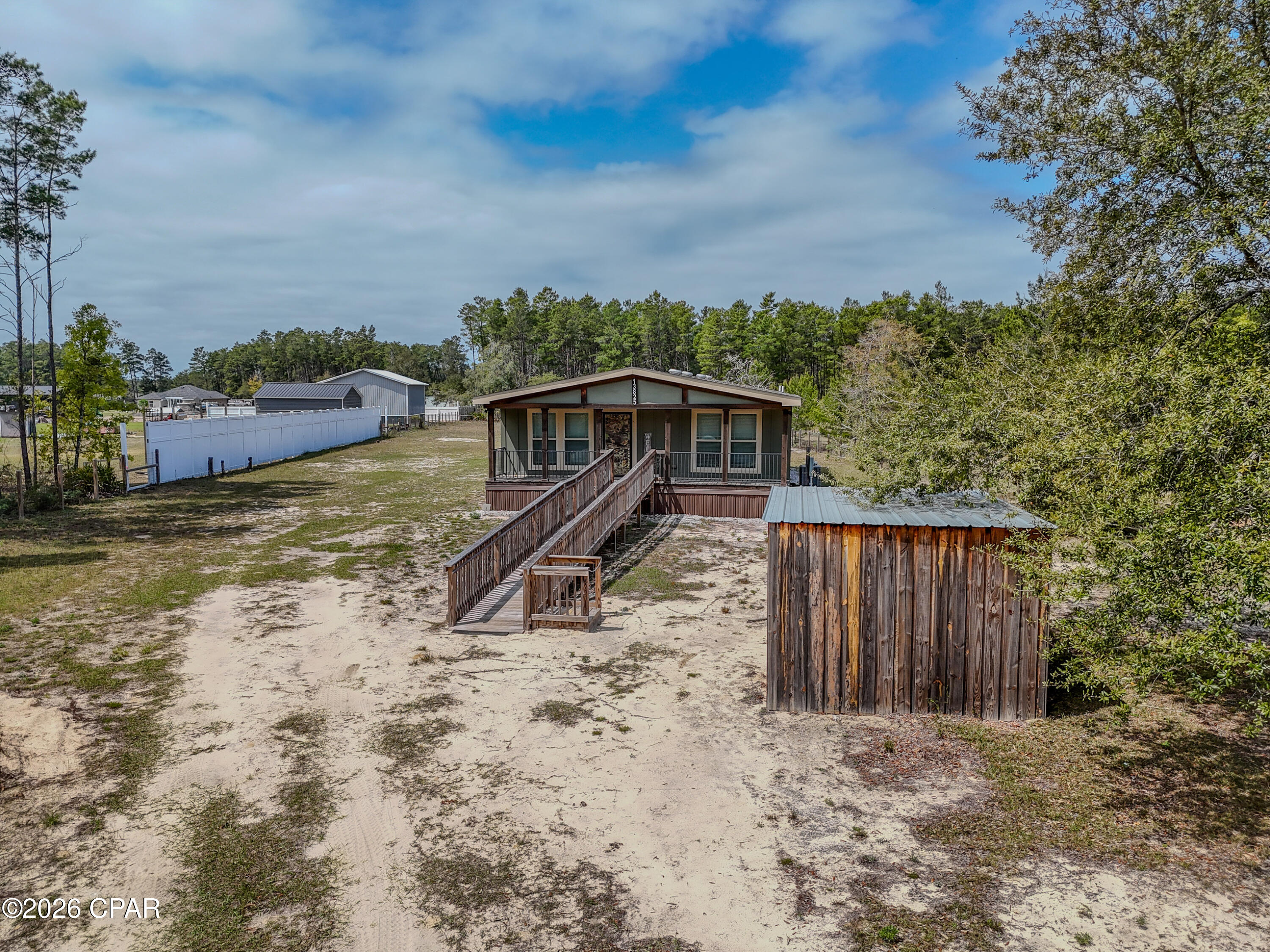 Welcome to 13825 Ashton Way in Southport, Florida, a custom 2021 Native Living Series Mossy Oak model by Deer Valley Homebuilders, thoughtfully designed to bring the beauty of the outdoors into everyday living. This ''Robin's Nest'' floor plan offers 3 bedrooms, 2 bathrooms, and approximately 1,920 square feet of well planned space within a 32 by 68 layout.

Set on a fully fenced approx. 1.033  acre lot, this property delivers the feel of true country living with room to spread out and enjoy your surroundings. The 30 foot covered front porch creates a welcoming first impression and the perfect place to relax in a rocking chair or porch swing and take in the peaceful setting. Around back, the 15 by 12 covered porch just off the dining area offers an ideal space for entertaining, grilling, or unwinding at the end of the day.

Inside, the home features a rustic yet modern interior with an open concept layout designed for both comfort and functionality. The living room is anchored by an electric fireplace, adding warmth and a cozy focal point. The kitchen is both beautiful and practical, showcasing rich wood cabinetry, granite countertops, stainless steel appliances, and a large center island with custom wood detailing. A large stainless farmhouse style sink adds both function and character, while wood beam accents, open shelving, and designer lighting tie the space together and reflect the nature inspired design this home is known for.

The primary suite offers a spacious and comfortable retreat with a double vanity, generous storage, and a thoughtfully designed bathroom. The oversized tiled shower includes built in seating and grab bars, blending style with added functionality. Additional bedrooms provide flexible space for guests, a home office, or hobbies.

Designed with accessibility in mind, the home includes custom ramp access at both the front and rear, providing convenient entry options. A custom built shed remains with the property, ideal for storing yard equipment and protecting the well from the elements. The additional backyard shed does not convey and will be removed prior to closing.

The Mossy Oak Native Living Collection is crafted for those who appreciate nature and want their home to reflect that lifestyle, combining natural textures, warm finishes, and modern convenience. Enjoy the balance of peaceful surroundings and everyday convenience with approximate drive times of 35 minutes to Tyndall Air Force Base, 20 minutes to Northwest Florida Beaches International Airport, and 25 minutes to emergency care at Ascension Sacred Heart Bay Emergency Room.

Schedule your private showing today with a REALTOR® and experience the feel of this home in person. If important, please verify all measurements and information. The additional backyard shed does not convey and will be removed prior to final sale.