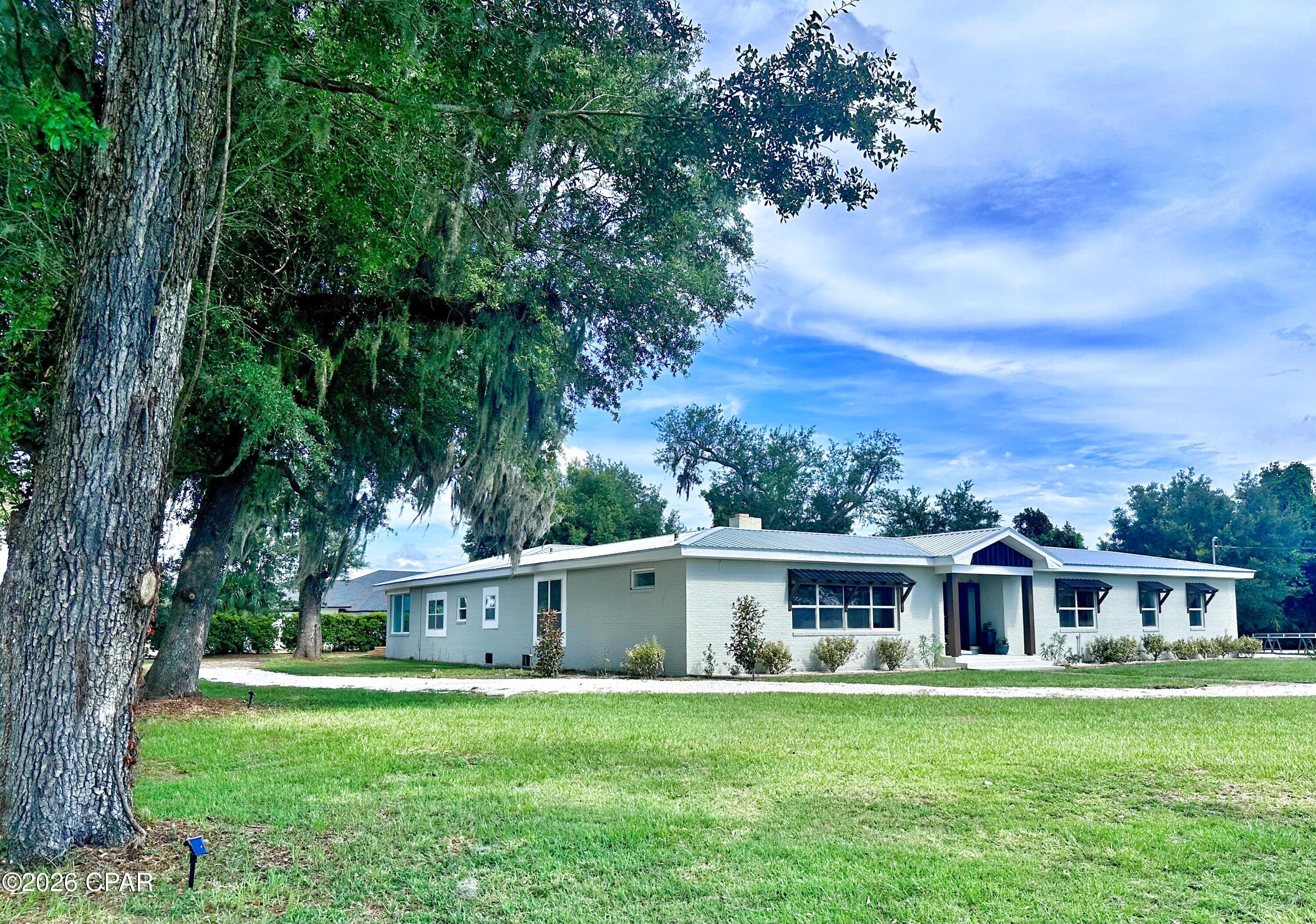 Forget cookie-cutter houses-- this lovely mid-century BEAUTY situated on over an acre in Lynn Haven is one of a kind; timeless craftsmanship with thoughtfully updated luxury. Brick pavers in the foyer immediately draw your eye to the centerpiece of the home: a spectacular atrium courtyard the very center of the home, complete with a built-in waterfall fountain and ideal for an outdoor kitchen, private herb garden, or just a relaxing retreat that can be accessed from several points in the home. Vintage oak hardwood flooring is featured throughout (no vinyl here!) and two gorgeous wood-burning fireplaces grace the living and family room. The chef's kitchen is designed to impress, offering a large granite-topped island, premium appliances, a farmhouse sink, abundant cabinetry, and a walk-thru pantry-- all overlooking the tranquil courtyard. Perfect for entraining, the home features a private guest suite tucked away from the family bedrooms, along with a convenient half bath just off the expansive living room. Each secondary bedroom opens into a heated and cooled sunroom spanning the entire back of the home, offering endless possibilities for a playroom, home office, fitness space, or simply a bright, relaxing place to unwind. The primary suite enjoys peaceful views of the sprawling side yard beneath beautiful moss-draped oak trees and features a spa-inspired, ultra-modern wet room complete with a soaking tub, dual shower towers, and a backlit vanity mirror. Built with solid concrete block-- a level of durability rarely found in newer homes-- and topped with a metal roof installed in 2024, this exceptional property offers the perfect combination of enduring quality, architectural character, and modern comfort. No HOA; conveniently located, plenty of room to spread out and enjoy.
