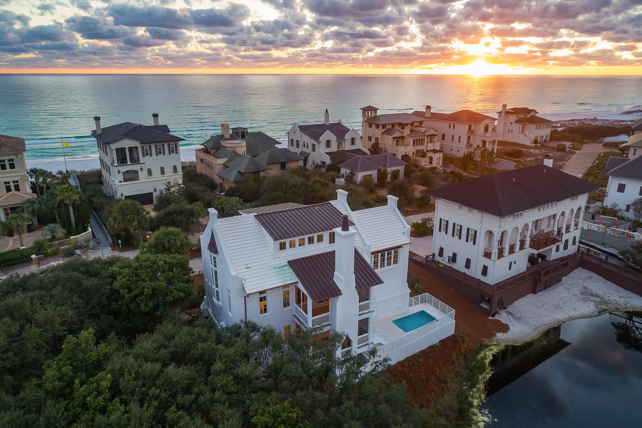 Located on the western end of 30A, the carefully planned, private, non-rental community of Stallworth Preserve, with stunning gulf and lake views. This new construction residence, by master builder Matt Fuller can be found just beyond the gates.
Upon entrance to this 4,350 square foot unique villa, the eye is immediately captivated by the brass inlay of the foyer's herringbone floor. This residence enjoys a reverse floor plan with guest suites on the lower level to fully expose the second floor living area which is surrounded by views and a custom pecky cypress ceiling creating a luxurious setting for entertaining and family gatherings. The cypress overhead flows seamlessly into the kitchen where the vaulted ceiling above commands attention, with luxury finishes and suite of Sub-Zero & Wolf professional appliances ensure that from the first toast to the final bite, guests and family alike will relish every moment and meal they partake in. The third-floor master suite can be accessed by the elevator and provides the perfect retreat after a day on the beach.
Throughout the residence reclaimed hardwood flooring and custom-built interior doors all crafted from French Oak imported from France add indulgent finishes throughout the home. The addition of salvaged beams ensures the custom touches to be expected of a luxury home. Each home elegantly draped all in the latest styles and designs. Designer tile, custom artisan cabinetry and Venetian plaster give each room in this villa a unique personality, while the oversized windows flood the home with light complimenting the visual comfort lighting throughout. The second-floor outdoor seating area is warmed by the tabby clad fireplace and overlooks the coastal dune lake as the ideal backdrop for your evening wine or morning coffee.
Quiet boutique community, private beaches, and fine architecture are just some of the features which ensure a superior quality of life at Stallworth Preserve and is only a few minutes away from the activities along 30A.