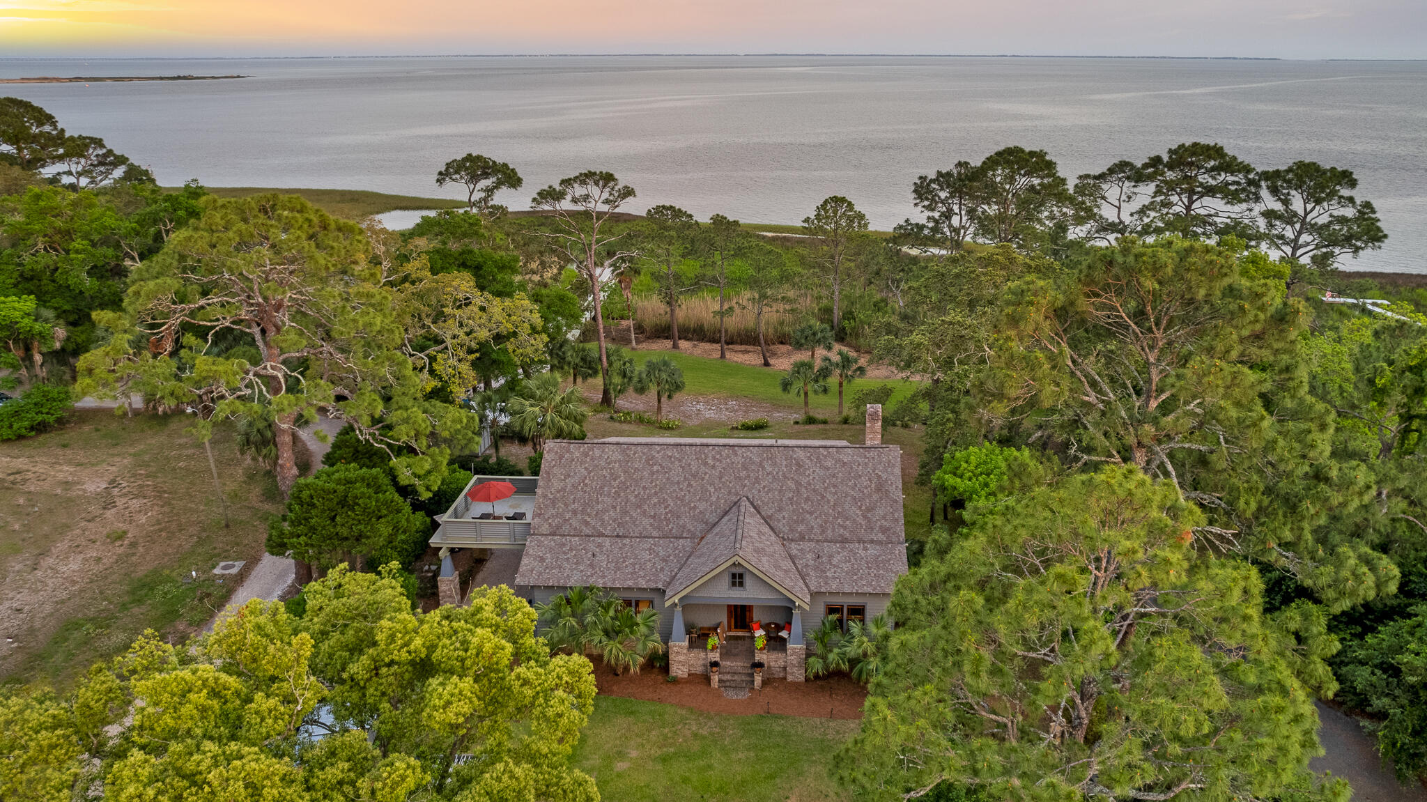 This Exquisite Private Compound, hosts a large, 5 Bedroom, 5 Bath,
''Craftsman'' Bungalow on an Acre on the Bay of Apalachicola, with private dock,
two guest studios, outdoor ovens, fruit orchards, gardens and spectacular
panoramic views of three barrier islands.
This exquisitely CUSTOM ''Arts & Crafts'' Bungalow was built in 2005, by the
current owners. The main house is a sculptural masterpiece, built of stick frame
construction on a slab, with cedar shake exterior, sitting on an acre on the
Apalachicola Bay, with view of SGI and barrier islands, with guest studios and
private dock.
The interior board and batten paneling, all doors and windows are made of clear,
''dead head'' cypress, in the Japanese influenced ''Arts & Crafts'' & ''Prairie Style.'' The owner/builder had antique logs (that had previously fallen off logging barges traveling up the Apalachicola River) pulled from the river by divers and local "dead headers." The cypress logs were aged and seasoned, then custom milled at Santa Rosa Mill Works. The floors throughout the house are of heart-pine and
provide incredible warmth and texture to the walls of one of the downstairs bedrooms, as well. Highly skilled finish carpenters, wood workers, cabinet makers, masons, stained glass artists, each blessed this remarkable home built of rare wood and custom materials. The are custom, hardware and built in mica lamps. The custom details of this gem are evident everywhere you look.
The house has a 5 bedroom, 5 bath floor plan, with an additional room distinctively an office or nursery. The large upstairs primary suite has a sitting room, large walk-in closet, Jacuzzi tub, and sauna. An upstairs stargazing balcony is off the entertainment/den area, which may also function as a sixth bedroom. The dormer spaces are insulated against temperature changes, which makes forlarge storage areas. The two downstairs bedrooms each have full baths. The built-in features arevremarkable; the stairs, staircases, newel posts, benches, bookcases, are all made
of deadhead cypress. The fireplace is framed by handmade "Green Man" art tilesvby an artist in Port Townsend, Washington. The four stained glass windows were fashioned by local Apalachicola artist, Paula Harmon. The kitchen has heart pine cabinets, lined in cedar and the stunning green subway tile, frames a six-burner gas stove. The counters are all hewn from 'heart pine, also, inviting the outdoors in. The chef's kitchen is highly functioning with
stainless appliances. Each floor of the guest house is totally autonomous, with private baths and kitchens. An outdoor free standing brick bread oven sits amongst citrus and fig orchards, organic garden, outdoor pergola and dining. A sweeping front Bay view porch overlooks the compound and the firepit on the Bay, for those memorable family evenings. The compound is home to over 250 species of birds, fish, dolphin, manatee, gators and otters.
Besides its unique beauty, the main feature of the home is its privacy. The property sits on over an acre on the Apalachicola Bay, on nine lots. The dock extends into the bay and is perfect for launching shallow draft watercraft. The property boasts views of three Gulf barrier islands: SGI, Little SGI and St. Vincent.
The house is on a high bluff, with stupendous views from every window. The property has both city and well water sources.