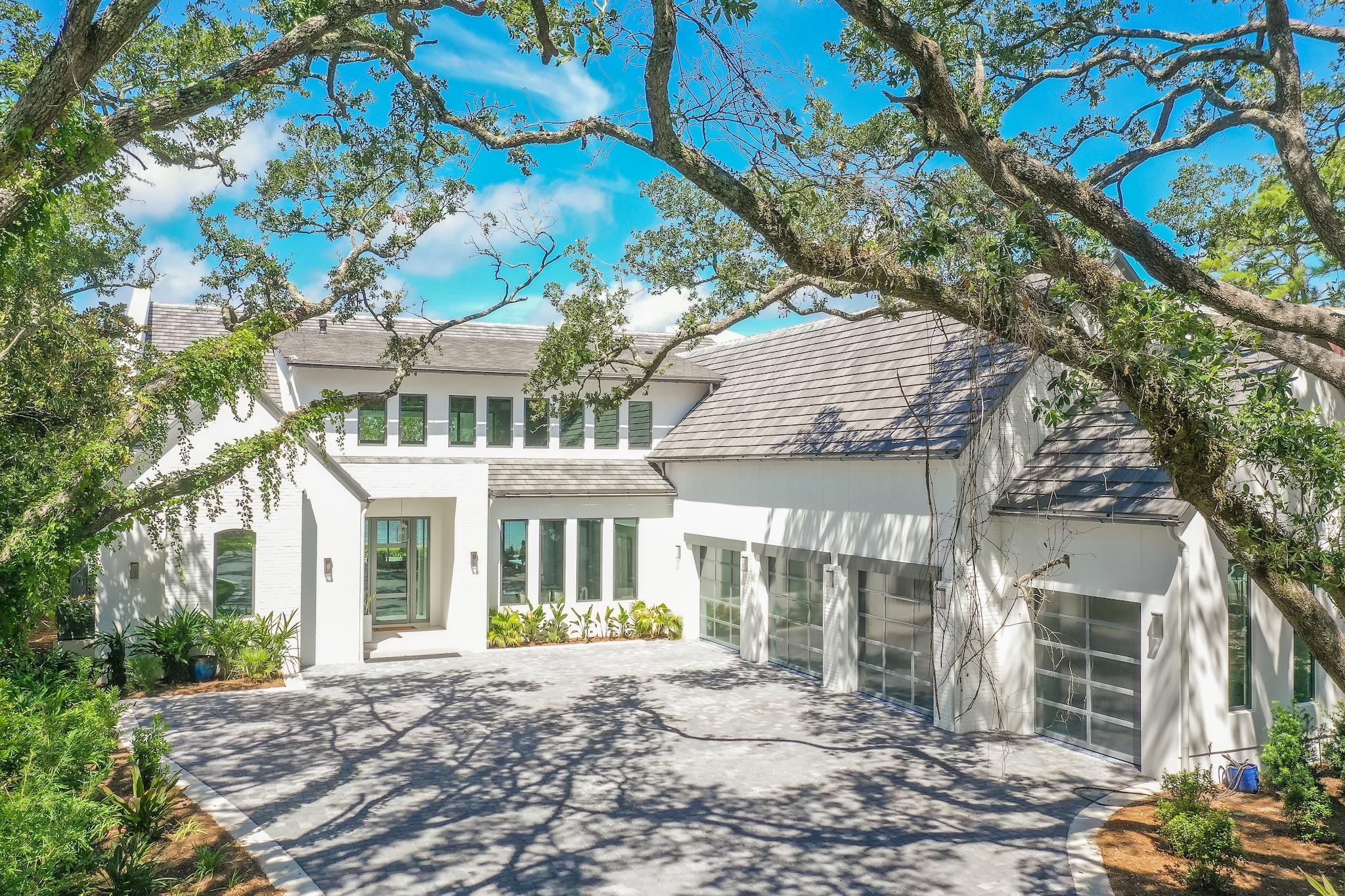 An extraordinary, nearly newly constructed, soft-contemporary dwelling stands poised among a covering of moss-draped live oaks and mature native landscaping. This home claims momentous presence over breathtaking 180 degree Choctawhatchee Bay views and year-round sunsets. A stately white stucco exterior softens under accents of painted brick, and pecky cypress. A dramatic wood and glass fully hinged front door hints at the well-appointed interiors while a 4 car garage is attractively accessed through full-view steel and glass retracting doors. Breathtaking bay views lure visitors through an unforgettable two-story wall of windows and fully retractable glass doors. Cool covered rear patios and contemporary glass framed balconies invite long evenings over low sunsets while a sensual resort-style pool, hot tub, sunken fire pit, and outdoor kitchen provide an at-home adult and kid-friendly playground. Dramatic interiors are draped by inspired 24' ceilings in the main living area. Ultra-modern light fixtures are softened by reclaimed ceiling beams and custom milled wood floors throughout. Naturally finished 10' wood paneled doors further soften contemporary themes while a dramatic steel walkway with glass handrails adds industrial modern flair. A striking two-story fireplace is tastefully shrouded in steel and natural stone. Deep blue and white European floating cabinetry is central to the open concept kitchen while a convenient quartzite lined dining island invites casual gatherings. Designer appliances include a Wolf range and built-in wine storage. Electronic enhancements include full-house SONOS sound, remote Lutron operation of all housing enhancements indoor and out, and electronic blinds in master and office areas. An expansive main-floor master suite rests Bayfront with retractable doors over a private patio. The master bath and baths throughout the home are fresh and modern with remarkable floating cabinetry. Bathroom tile patterns are intriguing; earth tones join grays and whites in memorable themes. An inspiring glass-walled, bay front home office flanks the home's west elevation. An additional bedroom/ bath, powder room, and expansive laundry complete downstairs living. A light-filled upstairs provides spacious quarters for guests including a second bay front master suite currently used as a fitness room. A plush, professionally designed screening room is lined with soft leather seating. Driftwood Road's Bayfront offers expanded bay front lots, and limited HOAs. Only minutes from Sandestin Resort and Grand Boulevard shops and dining, Driftwood Road is a renowned area for memorable architecture and Bayfront living.