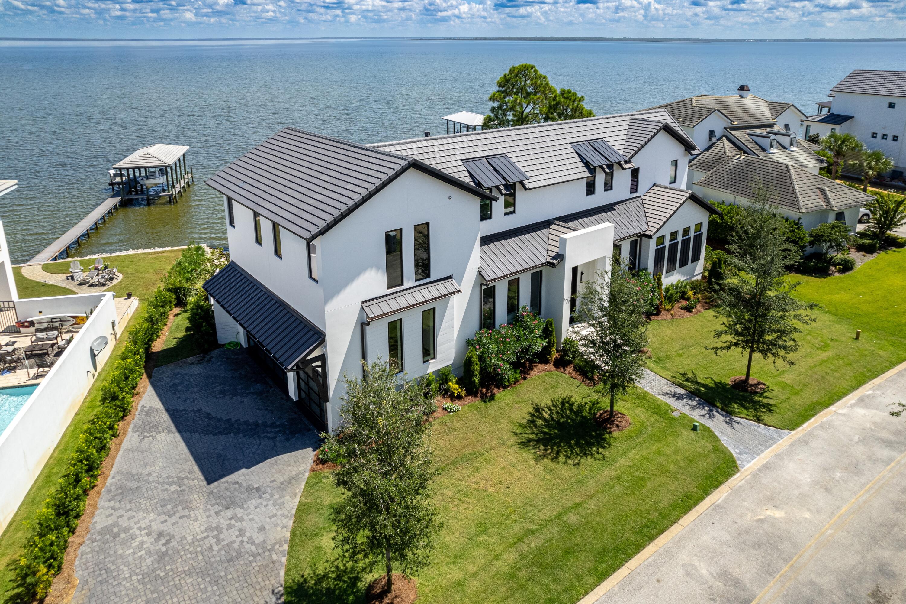 Sweeping bay views blend seamlessly with walls of glass in this 2023-built modern
stunner. Behind the gates of Driftwood's Grand Cove, this oasis of tranquility sits
majestically on 100' of private bay frontage with dock permit in place. First floor's open concept floor plan overlooks the water through 12' custom glass sliders. Tiled decking incorporates a cascading pool with sunken hot tub and a whimsically tiled grilling area.  The chef's kitchen parades deep hues of gray on black in sleek Marquis cabinetry, gleaming quartz counters, and brass hardware. The spacious island houses a notable black sink and seats a crowd. Designer appliances include a 48'' Aga custom gas range, Liebherr refrigeration and wine cooler with a Miele plumbed coffee maker. A wet bar with beverage station and ice machine serves guests and provides abundant storage. A
convenient scullery with storage is neatly tucked behind the main kitchen . A striking
dining room flanks the kitchen and enjoys its own water views, The entire home is
accented by naturally finished sold hard woods, designer lighting, and ceiling mounted
solid wood accent beams. The spacious living space is open to kitchen with a striking
floor to ceiling an arresting black metal fireplace with a 72" Napoleon gas fireplace. An
airy primary suite rests with a sophisticated wood accent wall conveniently on the first
floor with sunrise just outside it's full wall of windows. An alluring bath adjoins the
master with floating cabinets, attractive tile work, a shower enclosure with soaking tub,
and a roomy master closet designed by California Closets. Upstairs, all roads lead to
fun and privacy. A secondary living space with its own wet bar serves guests while three
additional ensuite bedrooms, one with a waterfront balcony, provide rest and comfort.
An impressive sound-proofed home theater room with a top of the line JBL surround
sound system provides hours of movies and music. The home is served by a climate
controlled three-car garage with stunning Glass garage doors. Two Rinnai gas hot
water systems separately serve each flank of the house. Flat screen TVs and Sonos
system to remain. Storage is well-placed throughout the home. Driftwood Road is conveniently located just minutes from Sacred Heart Hospital, shopping and dining in Grand Boulevard, and Sandestin Resort.