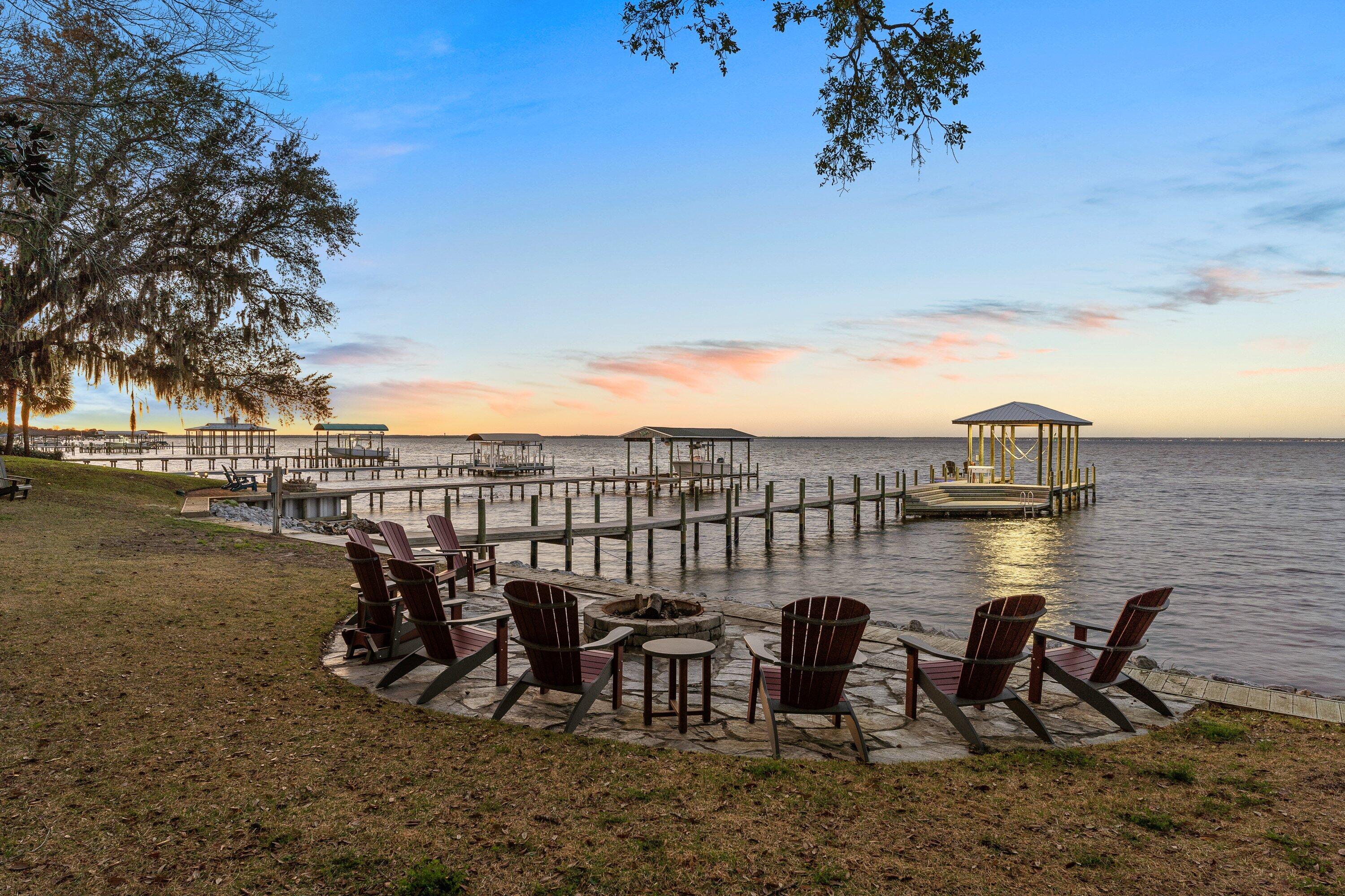 On a rare double lot with 200 feet of bay frontage, this fully updated brick estate is positioned down a gated, circular driveway between a canopy of mature oak, magnolia, citrus trees, and crepe myrtles. Built for entertaining, the expansive backyard is perfectly framed with stately live oaks surrounding a deep saltwater pool and oversized hot tub. Take in picturesque, year-round pool to bay views from several rooms in the house. Enter the foyer to an elegant curved staircase, where the well-thought out floor plan and thoughtful updates promote easy living and ultimate privacy. The master suite is positioned on the second floor for maximum views, and boasts a spa-like bathroom with a freestanding tub and separate shower with a rain head, separate hand sprayers, and multiple body sprayers. The living room features a wet bar with a 50 gallon ice maker and wine refrigerator. A large center island anchors the kitchen, which boasts Wolf appliances and French doors leading out to the patio.  Walk upstairs to find two master suites, a laundry room, and two guest rooms. Brand new roof installed in February 2023 with a premium lining. In addition to the main house is a detached two car garage; a third bay that was finished to be a bedroom and full bath; a cabana with a full bathroom, grill, and smoker; a potting shed with electricity and a new roof; as well as a gazebo with electricity. All new Anderson storm doors and windows, garage doors, wrought iron railing, outdoor fans, flooring, and paint. The sea wall and dock with 8,000 lb boat lift were constructed in the last five years, and the hot tub was constructed in the last four years, along with a pool resurface and new equipment. Capture dreamy sunsets over the bay by the firepit with soft cafe lights leading back to the pool terrace. This is bayfront living!