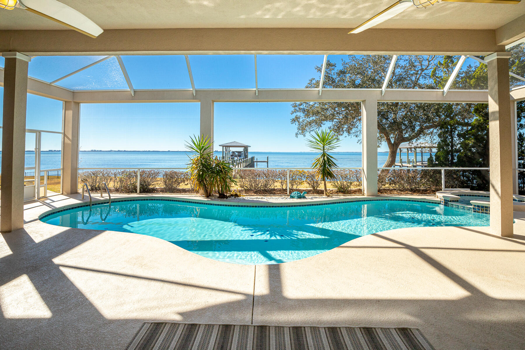 Accepting backup offers! A beautiful bayfront setting in the gated Southwind community of Bluewater Bay offers year-round sunset views from almost every room. Experience the timeless features of this custom home with thoughtful upgrades and impactful finishes. Find 9-12 foot ceilings and an open floor plan to highlight the three sets of glass doors which open to the screened-in pool, spa, and fountain, and the bay beyond. A remodeled gourmet kitchen includes a gas cooktop, wine cooler and ice maker. Enjoy coffee from a built-in banquette in the kitchen as you watch dolphins play in the distance. New flooring throughout. The master bedroom offers pool and bay views, while the master bathroom features separate vanities, a walk-in shower and soaking tub. Entertain year-round on the back patio with a covered porch and screened-in pool, and a spacious lush lawn along the bay. The pool has been re-plastered and the heater has been replaced within the last five years. A half-bath serves pool guests. Enjoy convenient one-level living, plus a fourth bedroom/bonus room which is also accessible by a separate upstairs entrance. The roof, boat dock with boathouse and driveway were replaced within the past year. There is a two car garage, plus extra golf cart storage. Bluewater Bay offers several membership amenities such as tennis, golf and a marina.
