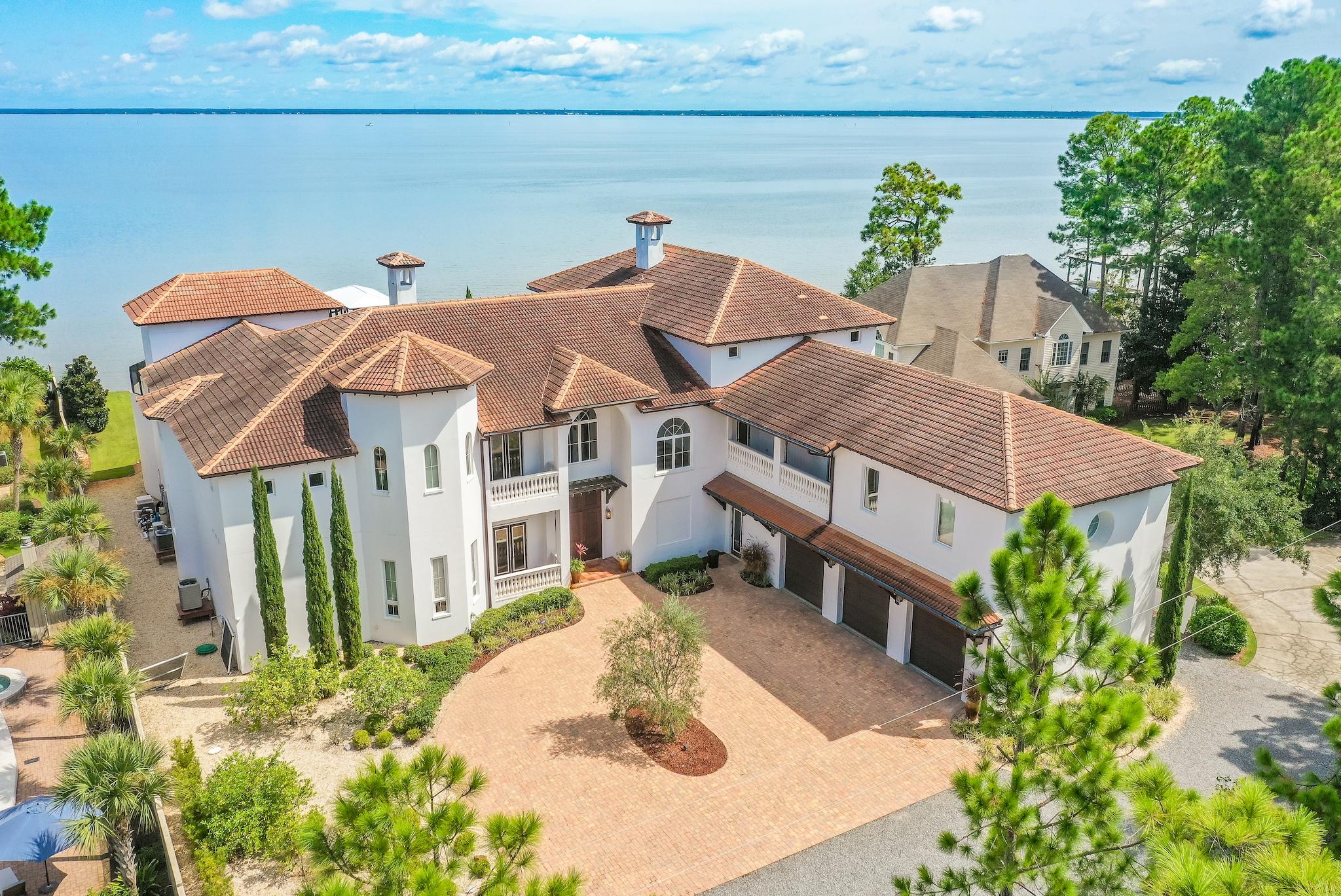 This architecturally distinct 14,000 square-foot residence takes full advantage of its bayfront location, blurring the lines between indoors and out while allowing for the most pleasurable resort-like lifestyle. The breezy outdoor spaces and light-filled, view-focused interiors offer relaxed and refined modern living.
With over 130 feet of water frontage on the Choctawhatchee Bay, the property boasts a private boat lift and dock leading from the water to the estate's lavish amenities which include an outdoor kitchen, pool, hot tub, and screened-in lanai. A generous green space offers additional room for entertaining guests, family holiday celebrations or large-scale corporate events.
Beyond the French doors, an open floor plan reveals expansive light filled living spaces. Rich details abound including stunning hardwood floors, 25-foot ceilings, and an abundance of windows showing stunning views of the Bay, pool, and pool deck. The chef style kitchen has custom cabinetry with a suite of professional grade appliances and a butler's pantry. Among the mix of formal and casual spaces, the room is anchored by the gas fireplace with custom mantle, a second wine fridge and ice, additional living spaces, and formal dining area. Adding to the list of amenities is the large 1st-floor primary bedroom oversized walk-in closets, private access to the courtyard and spa-like ensuite, featuring a walk-in shower, soaking tub, dual vanities, and additional powder room.

The second level of the home offers a 2nd-floor suite and loft area with water views, private fireplace, and ensuite complete with sauna and large walk-in shower.  Two additional guest suites can be found on the second level, offering an oasis after a day on the water with private balconies overlooking the Bay.  A bunk room with ensuite completes this level.
 
An elevator makes accessing the upper levels of the home simplistic, where third-floor views await behind a wall of windows.  Enjoy your nightcap or sunrise with coffee from the morning kitchen. A carriage house with full kitchen and living area offers the ideal guest retreat and offers access to a shared balcony.
 
Notable features of the home include: hardwood flooring throughout, custom drapery, marble fireplace, and columns, splash pad and lush landscaping.