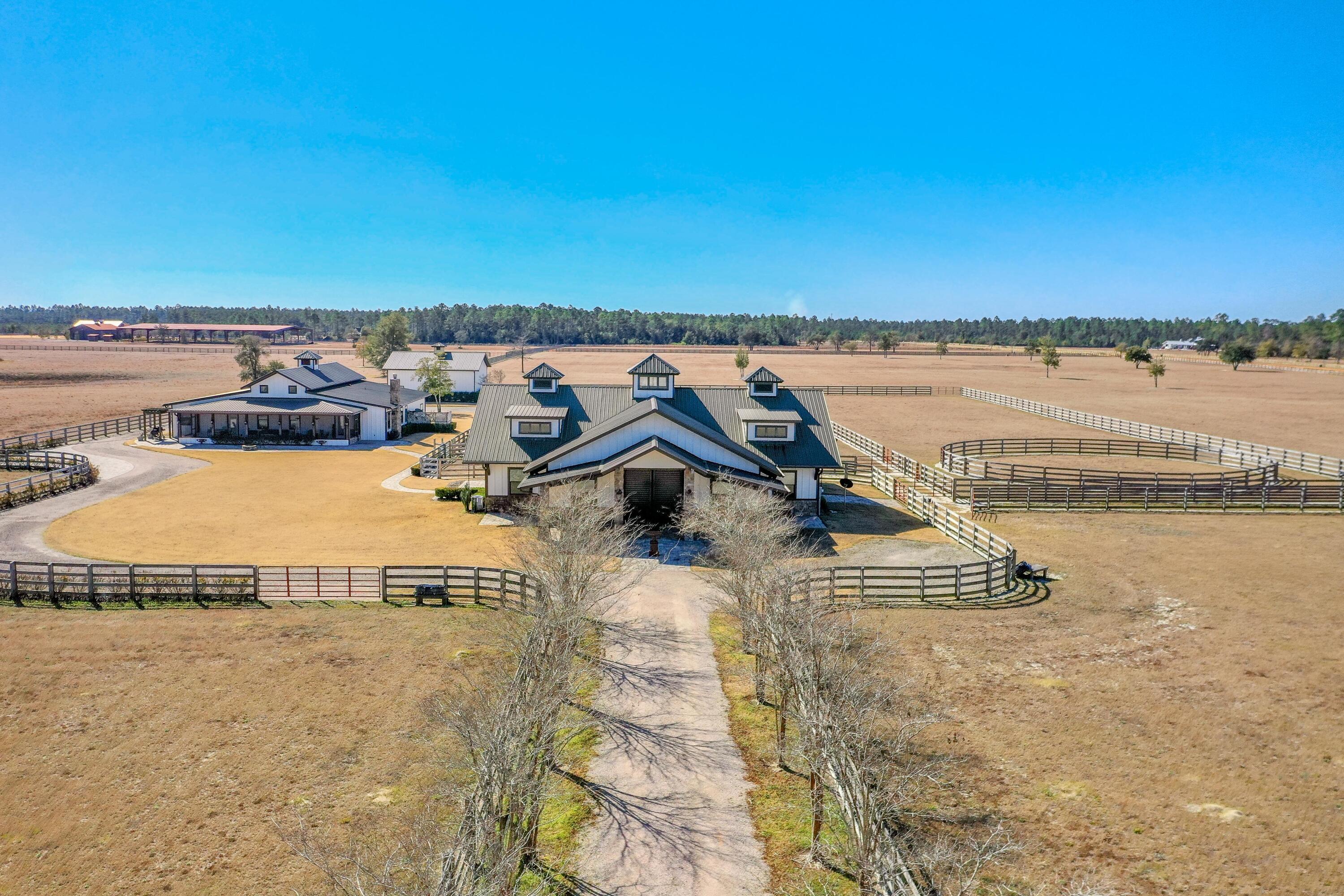 The elite equestrian community known as the Stables at Sandy Pine accommodates a horse-lover's dream lifestyle.
This subject assemblage of four prime parcels of Walton County, Florida is located within an approximate 50-minute drive to the beaches of South Walton County and Scenic 30A of Santa Rosa Beach, Florida. This is a fully turn-key opportunity, including all furnishings, electronics, and entire utility building of farm equipment, including a tractor, bush-hog, zero-turn professional riding mower, atv's, etc. The finishes throughout are nothing short of extraordinary, rivaling world-class barns fit for the finest of thoroughbreds. Each of the six stalls offer the horses deluxe accommodations, including double-rotating fans, automatic watering bowls, anti-fly misting system, and... a covered paddock.  There is a beautiful secondary kitchen and bathroom that serves the barn, as well as a large study, separate wash area and tack area.  The metalwork, woodwork, and overall design of the barn is perfection.  The main home offers an enormous expansion of covered space that is currently an oversized garage, which could easily be transformed into another 2-bedrooms and bathrooms, yet still yielding a garage space and an enormous bay that was designed to accommodate a Prevost motorcoach with hookups and rolling ladder, reaching motorcoach heights.  The interior of the main home features beautiful finishes as well, including custom cabinets, gorgeous stones and tiles, and fabulous millwork.  The front screened porch is expansive and features a covered hot tub.  The manicured pastures are strategically fenced with versatile gates allowing for the convenience of accommodating various turnout scenarios in the pastures.
The exterior improvements, including the lush landscaping and hardscaping design, are gorgeous.
The improvements were constructed in 2014, so the metal structural aspects are impressive, including its use of products, such as spray foam for insulation, which reduces utility costs.  Please inquire for further details and to schedule a private showing with a minimum of 72-hour advanced notice.  The listing agent(s) must accompany all showings.