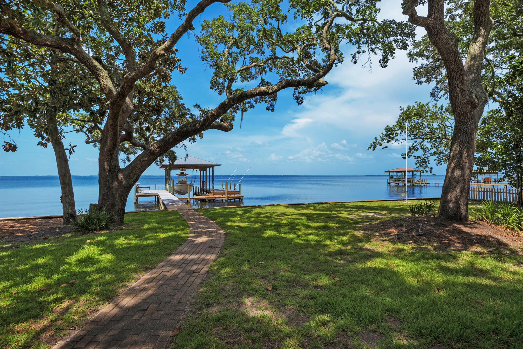 Privacy on the bay! 100' feet of tree-lined frontage and views for miles with this bayfront home and separate carriage house. A detached, screened-in summer kitchen overlooks -1/2 acre of beautiful oaks, magnolias and pines. The interior of the main house has 3 bedrooms and 4.5 baths. The updated kitchen is open to the living areas and takes full advantage of the stunning water views. A climate-controlled garage will accommodate 3 vehicles. The recently updated carriage house contains a full kitchen, living room, bedroom, bath, and laundry. The dock and boat lift will accommodate up to a 9000 lb. boat and includes a jet ski lift. Great year-round water access for most boats. This home is currently under contract.Showings may be allowed with proof of ability to purchase.