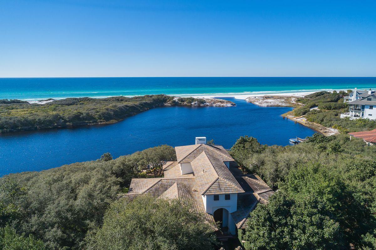Masterful concrete construction paired with a rich historical and architectural significance characterize this exceptionally located beachside retreat in the exclusive gated enclave of Redfish Lane. Primely positioned on .82 acres of land, this rare estate-sized property provides an astounding 220' of water frontage perched on an elevated bluff overlooking the Gulf of Mexico and Little Redfish Lake with insulated privacy from the majestic dune topography at Grayton Beach State Park allowing for an unparalleled naturescape. Originally built in 1994 and beautifully rendered by Christ & Associates Architects, this timeless coastal retreat is both sophisticated and structurally sound with an extensive renovation by Galvas Construction completed in 2011 yielding a new tile roof, new impact windows & doors, updated kitchen & baths, new HVAC units as well as highly curated finishes and design details hand selected by Bohlert Massey Interiors. This four bedroom home was designed for entertaining offering an open floorplan and expansive living areas all focusing on naturalistic views of lush native foliage and european gardens that overlook Little Redfish Lake and the Gulf of Mexico. The primary living spaces can all be found on the first level of this well-designed retreat which allows for a welcoming sense of arrival through a pristine courtyard entryway and a grand foyer with double height ceiling. The finely appointed chef's kitchen embodies a cosmopolitan essence with elegant carrera gold marble countertops and sleek custom stainless cabinetry allowing for ample storage space as well as an impressive appliance package including double Miele dishwashers, double Wolf wall ovens, Viking fridge & freezer and a sizable gas cooktop. The kitchen is adjacent to a spacious butler's pantry and open to a beautiful sitting area overlooking the south facing elevation with ample natural light from floor to ceiling glass windows as well as gorgeous architectural elements including a reclaimed wood ceiling. The main living room is characterized by beautiful herringbone wood floors and exemplary beamed ceiling anchored by a sizable gas fireplace and flanked by two office spaces with floor to ceiling glass architectural windows allowing for a timeless elegance and ample natural lighting. The first level also features three sizable bedroom suites each offering direct access to a beautiful ensuite bathroom all of which has been adorned with marble accents and hand-made brass plumbing fixtures. The master suite was strategically situated on the second story and solely occupies the entire floor offering an expansive view over Grayton Beach State Park and Little Redfish Lake while also creating a luxe space to retreat and enjoy the adjoining spa-like master bathroom complete with steam shower, dual vanities and spacious dual water closet. The master suite also offers a large walk-in closet as well as a sizable south facing covered porch allowing uninterrupted views over the Gulf of Mexico. Other notable features include an oversized two car garage, private parking court, serene koi pond as well as fenced privacy and lush manicured grounds with mature oak trees leading to a private dock with unimpeded access to Little Redfish Lake. Redfish Lane is located in the heart of Blue Mountain Beach Florida and is known as a private enclave of timeless, fortified residences nestled between Grayton Beach State Park and Big Redfish Lake. This prime location allows for the ultimate private sanctuary and retreat along Scenic Highway 30A while also offering excellent proximity to Seaside, Watercolor and all of the world class shopping, dining and entertainment that 30A is known for.