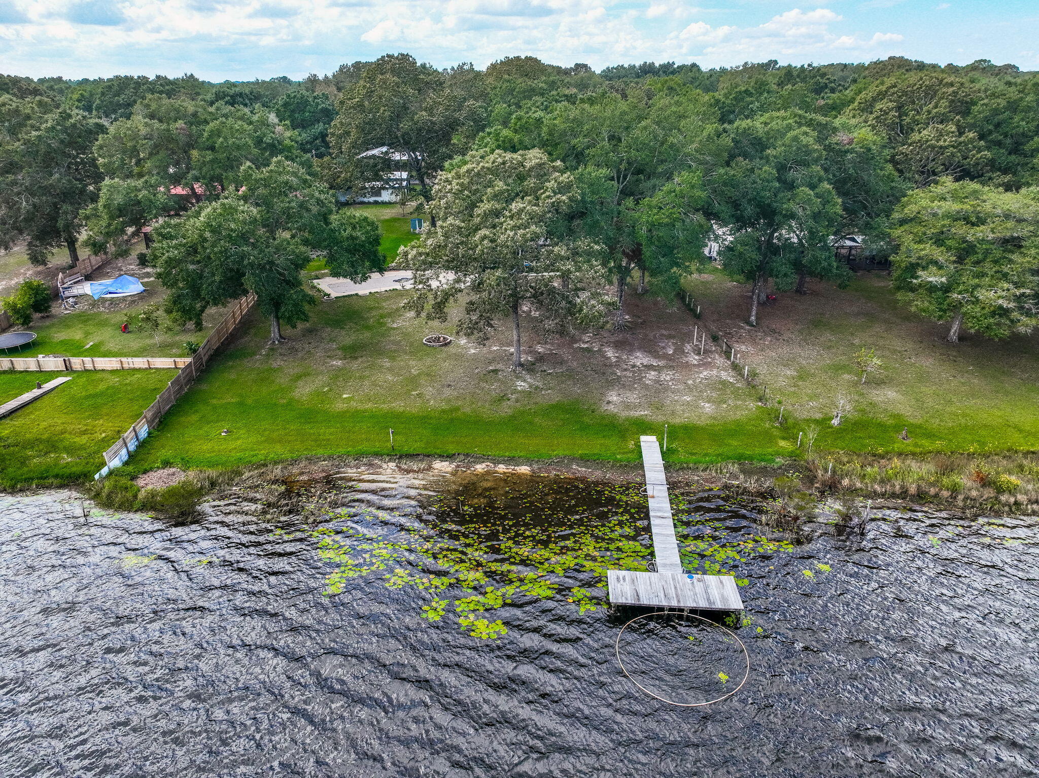 Rare opportunity to own a LAKESIDE RETREAT  nearly 2 acres of fully fenced waterfront property on Lake Holley, a 400-acre fishing lake known for trophy bass, bream, and bluegill. This two-story home offers a functional layout with a fully updated kitchen, tile flooring throughout the main level, and hardwood stairs leading to two spacious upstairs bedrooms. The main-floor primary suite provides convenient single-level living, and large windows offer peaceful lake views and natural light. A screened-in back porch overlooks the water, while the private dock is ideal for fishing, kayaking, or simply enjoying the sunset. A detached structure--formerly a she-shed and now accessed by a sidewalk--offers excellent potential as a lock-out guest suite, artist studio, or a short or long-term rental. Multiple outbuildings and covered carports offer storage, workshop potential, and parking for RVs or extra vehicles. With no HOA and endless flexibility, this property is perfect as a full-time residence, weekend getaway, or investment opportunity just minutes from DeFuniak Springs.