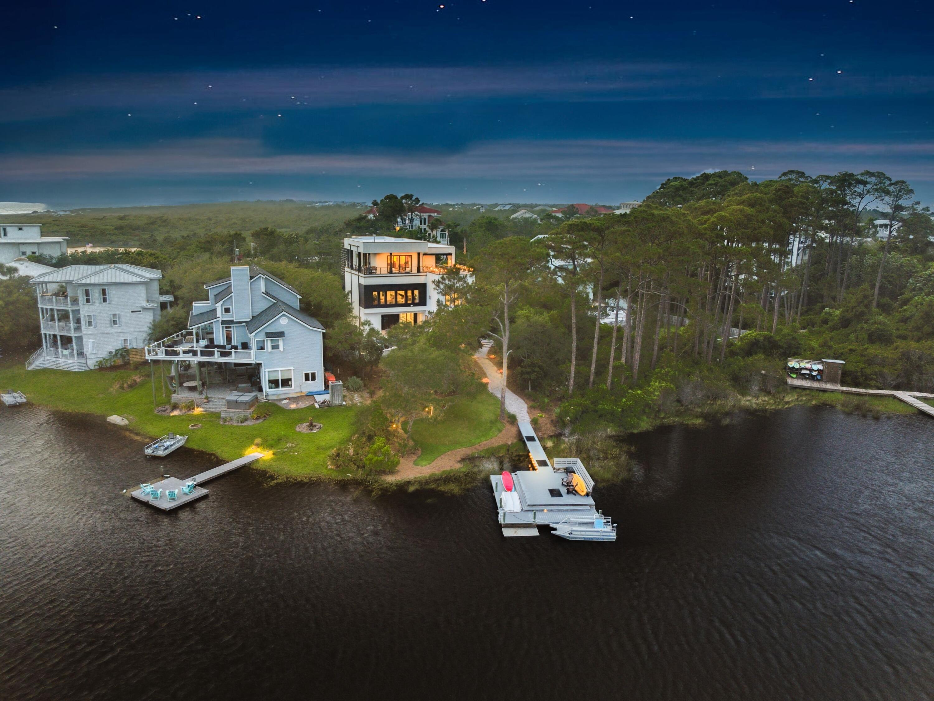 Step into a one-of-a-kind contemporary retreat where bold architectural design, thoughtful craftsmanship, and serene coastal surroundings converge along the tranquil shores of Lake Stallworth. Completed in 2023, this 6,200-sq.-ft. custom-built estate offers five bedrooms, six full bathrooms, three half baths, and a multi-level layout designed for luxurious living and effortless entertaining--just a short stroll from the sugar-white sands of the gulf and a short ride by boat to an exclusive beach. From the moment you enter the soaring atrium-style foyer, you're greeted by natural light pouring through glass walls, bringing the outdoors in and immediately setting a calm, sophisticated tone. On the first floor, a comfortable lounge and kitchenette create the perfect hangout zone, with sliding glass doors that open wide to a sprawling patio, saltwater pool, and hot tub. Just outside, a built-in putting green adds a playful yet polished touch to this impressive outdoor living space. Whether you're sunbathing poolside, cooling off with a dip, or gathering with friends on a breezy afternoon, this backyard oasis invites you to slow down and savor the moment. Also on this level are two beautifully designed bedrooms, including a custom-built bunk room that's both stylish and playful--ideal for hosting kids or extra guests with ease and comfort. From the back patio, a private boardwalk leads you to Lake Stallworth, where you can launch kayaks, enjoy sunset paddles, or take in the peaceful water views from the private dock. The second floor is the heart of the home and a true showpiece. Here, an expansive open-concept living room is anchored by a dramatic gas fireplace and surrounded by floor-to-ceiling windows that flood the space with natural light and frame the beauty outside. The vibe is refined yet welcoming--perfect for unwinding after a day at the beach or hosting evening cocktails. The chef's kitchen is custom in every sense, featuring granite countertops, a sleek stainless steel backsplash, and high-end appliances that blend form and function. A generous dining area offers space for long, laughter-filled meals and holiday gatherings. Also on this level are two guest suites, each with its own full bath and a private gym that keeps wellness and convenience steps away. The third floor is home to the luxurious primary suite, a true sanctuary in the sky. Wake up to sweeping gulf views and let the sound of the surf carry you to sleep at night. Step out onto the wraparound balcony, where an outdoor kitchenette with a side-by-side refrigerator/freezer offers the perfect setup for grilling and serving guests on the top deck. The spa-inspired en suite bath features sleek tilework, dual vanities, and a stunning glass shower. From this level, take the stairs to the rooftop observation deck, where the panoramic views stretch from the calm lake waters to the emerald coastline of the gulf--a perfect perch for sunset toasts, stargazing, or quiet reflection. This is more than a home--it's a custom coastal haven, designed for those who appreciate artful living, privacy, and the restorative power of nature. Whether you're entertaining, relaxing, or exploring the best of 30A, this one-of-a-kind estate offers a lifestyle that is both elevated and grounded in the beauty of its surroundings.