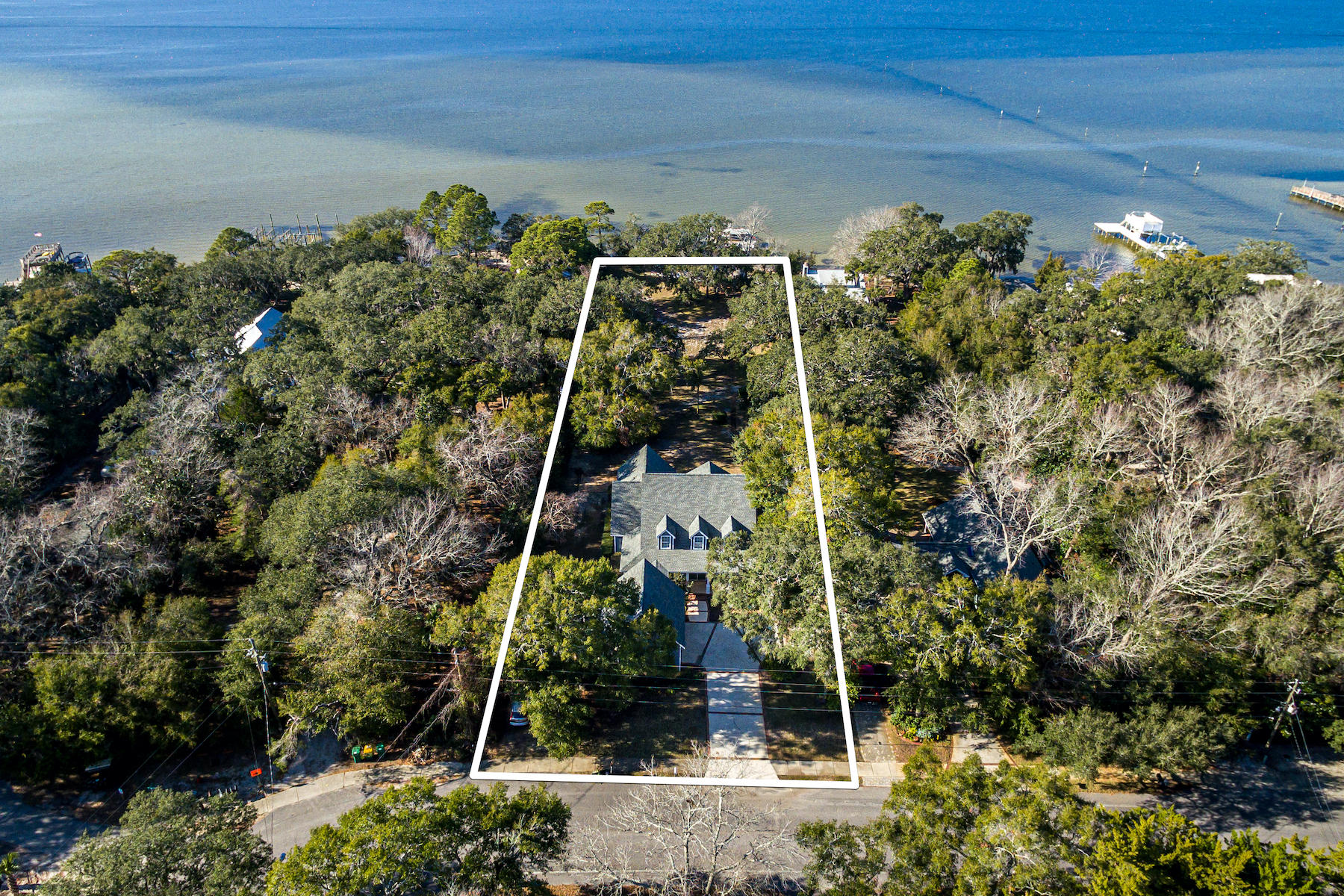 A cathedral of native oak trees drip with spanish moss on over an acre of welcome oasis, year round sunsets, and sparkling bay waters. Traditional southern architecture meets coastal chic in
this well-appointed four bedroom, four and a half bath bay-front home. This home invites relaxation beginning with the concrete and brick lined driveway and welcoming covered front porch,
through the large landscaped backyard, and ending past the waters edge. Destin's popular Crab Island and the sugar-white sand beaches of the gulf are mere minutes by boat through the East Pass. Two lots combine for 100' +/- of total bay
frontage and offer the opportunity to build a second dwelling on the eastern lot with 82' of frontage. A lofty two-story brick fireplace overlooks a wall of windows
and hearth serves as the focal point of the family room, complete with a wet bar for easy entertaining. At the heart of the home, the gourmet eat-in kitchen features a large island with plenty of cabinets, upgraded appliances, and a gas range. Stunning
Australian cypress flooring completes the warm tonal composition and could be expanded to all living areas. Custom-built bookshelves line an office wall while natural light pours in through
one of the many windows in this home. The master suite on the main level boasts a private patio and spacious attached master bathroom. Another full bath, dining room, and large laundry
room complete the main level. Three additional bedrooms, two bathrooms and a bonus room are found upstairs allowing for plenty of space and privacy for guests. Calhoun Avenue is a quiet neighborhood
conveniently located near Destin's Harbor front entertainment and dining complex.
