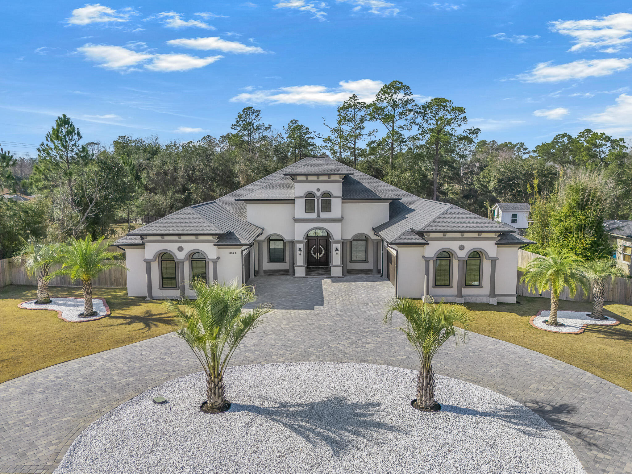 This exceptional, architecturally designed residence blends striking scale, thoughtful craftsmanship, & refined luxury into a home that feels impressive & inviting. Set on a 0.79-acre lot, the property immediately captivates w/its dramatic 24' front porch tower, soaring to a 32' roof peak—a bold statement that sets the tone for what lies beyond. Inside, 5,000 S/F of beautifully curated living space unfolds w/intentional openness and flow. Ceiling heights range from 10 feet to over 16'5'' in the Great Room, where custom ceiling designs, floating architectural walls, & a stunning 6-foot crystal chandelier create a sense of volume & elegance. A 45-foot open span & expansive 16-foot sliding glass doors invite natural light & seamlessly connect indoor living w/the outdoors. This exceptional, architecturally designed residence blends striking scale, thoughtful craftsmanship, & refined luxury into a home that feels impressive & inviting. Set on a 0.79-acre lot, the property immediately captivates w/its dramatic 24' front porch tower, soaring to a 32' roof peaka bold statement that sets the tone for what lies beyond. Inside, 5,000 S/F of beautifully curated living space unfolds w/intentional openness and flow. Ceiling heights range from 10 feet to over 16'5" in the Great Room, where custom ceiling designs, floating architectural walls, & a stunning 6-foot crystal chandelier create a sense of volume & elegance. A 45-foot open span & expansive 16-foot sliding glass doors invite natural light & seamlessly connect indoor living w/the outdoors. Every finish was selected for beauty and longevity. High-grade tile & luxury vinyl plank flooring extend throughout the home, front porch, & covered lanai, while 48-inch wide hallways & 8-foot solid doors enhance the home's grand, custom feel. The kitchen is the heart of the homeanchored by a statement 9'5" x 5' Dolomite island, dual glass-front refrigerators, custom cabinetry, & an elegant in-wall wine cabinet, making it equally suited for everyday living & entertaining. Five spa-inspired bathrooms elevate daily routines w/floating vanities, frameless glass showers, smart bidets, touch-free fixtures, & illuminated mirrors, offering a retreat-like experience throughout the home. Outdoors, the property transforms into a private oasis featuring approximately 6,000 S/F of pavers, a circular drive, privacy fencing, & meticulously curated landscaping with mature palm trees, Zoysia grass, & white marble stone accentsall supported by a dedicated irrigation system. With integrated security, mobile-controlled systems, and enduring construction throughout, this home is more than a residence, it's a thoughtfully crafted lifestyle, designed to be experienced, enjoyed, and admired for years to come.