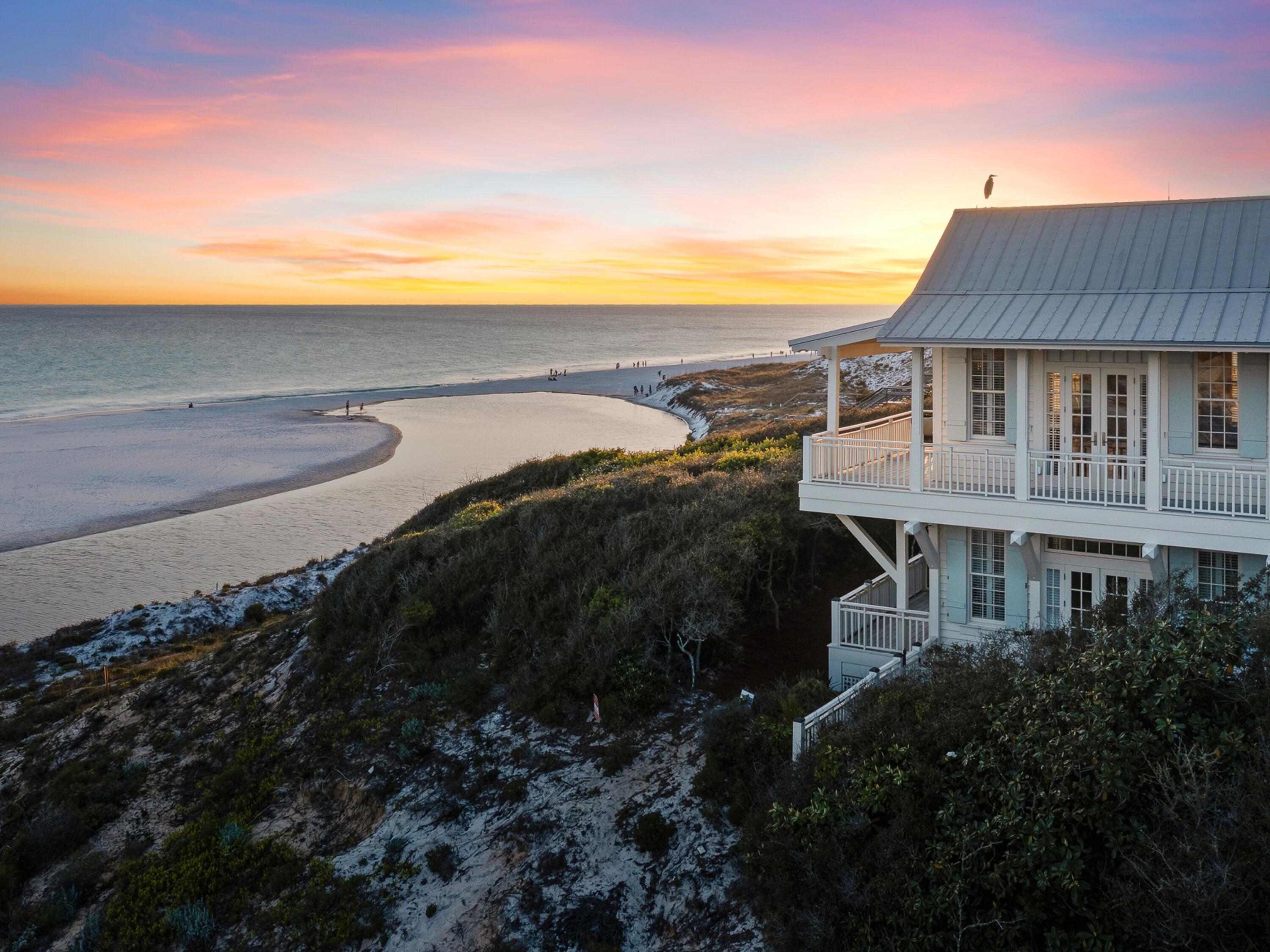 Rare even by 30A standards, this legacy property commands one of the most extraordinary settings on the coast, with Draper Lake and the gulf unfolding in a sweeping panorama that rivals any view along our coastline. This residence was designed to honor its remarkable homesite, pairing enduring construction with architecture that feels both stately and deeply connected to the landscape. From the moment of arrival, the experience is defined by elevation, light and an ever-changing backdrop of dune vegetation, lake outfall and open water. Built in 2006, the five-bedroom residence spans over 4,700 square feet of heated and cooled living space and rests on a homesite with an exceptional 245+ feet of combined waterfrontage. Engineered for longevity, the structure is anchored by deep wood pilings and reinforced by substantial retaining walls, a thoughtful response to its elevated coastal setting. A private elevator, whole-home generator, six-zone HVAC system and smart home integration provide a level of comfort and functionality that quietly supports everyday living. The home's Low Country-inspired architecture is expressed through cedar lap siding, a standing seam metal roof, copper-accented railings and expansive Brazilian hardwood decking. Inside, hand-hewn cypress floors, marble surfaces, tongue-and-groove cypress paneling and exposed cypress trusses create a layered interior rich in texture and craftsmanship. The main living, dining and kitchen spaces are crowned by a dramatic Cathedral ceiling with clerestory light, while walls of windows and French doors frame uninterrupted coastal views. The kitchen is both refined and highly functional, anchored by a statement La Cornue range, Sub-Zero refrigeration, custom cabinetry and a well-appointed butler's pantry. The gulf-facing primary suite opens onto a covered porch and features a beautifully detailed bath and built-in wall of mirrored closet doors. Guest suites are treated equally, each with a private bath and many offering direct access to outdoor living areas. Outdoor spaces are designed to complement the setting without competing with it. A private pool tucked behind native vegetation creates a sense of seclusion, while covered porches and elevated decks offer multiple vantage points to take in the view. A private dock and boardwalk extend to Draper Lake, offering effortless access for paddleboarding, kayaking and quiet mornings on the water. Within the gated community, owners enjoy multiple beach walkovers, a community pool and dedicated beach access. With frontage on both a coastal dune lake and the gulf, this is a unique location and elevation along Scenic Highway 30A.