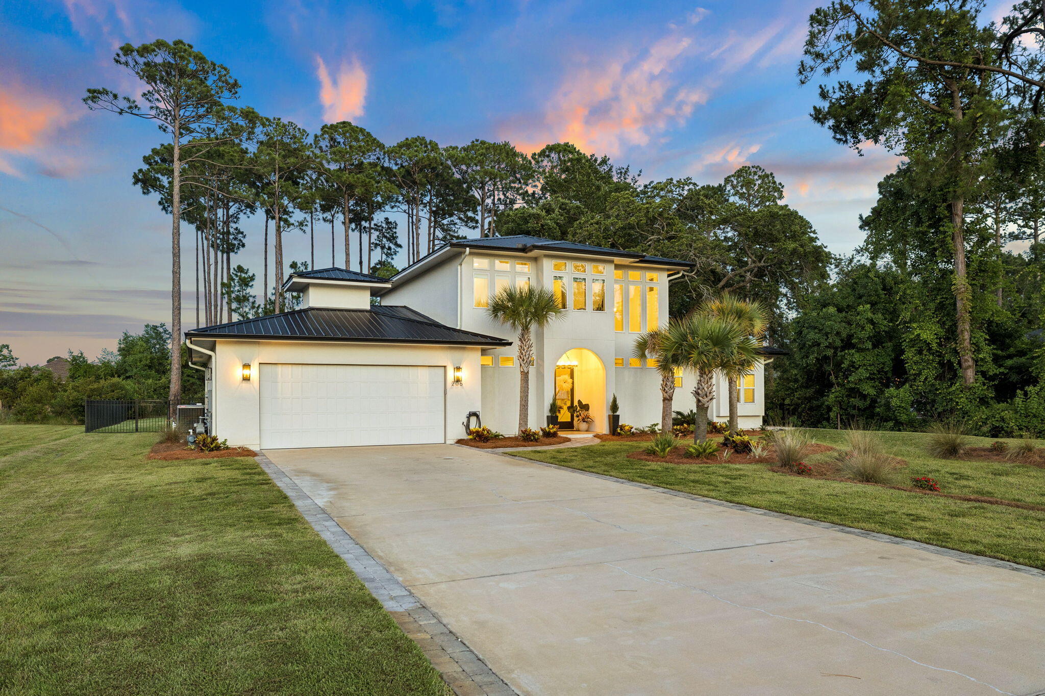 Coastal contemporary living comes to life in this two-story new-construction home, tucked among towering pines on a fully fenced bayside homesite. A standing-seam metal roof, clean stucco lines, and a paver drive make a refined first impression.

Inside, the chef's kitchen anchors an open great room with wide-plank white oak floors, soaring ceilings, and walls of windows. Custom shaker cabinetry, a quartz waterfall island, designer tile backsplash, gas range with vented hood, and statement pendant lighting flow to the covered patio through French doors. A new whole-home UV HVAC system keeps interior air clean.

The main-level primary suite offers a tray ceiling and spa-inspired bath with marble-look tile, a freestanding soaking tub, oversized glass shower, dual vanities, and a walk-in closet. A secondary bedroom, full bath, laundry, and oversized two-car garage complete the main level; upstairs are two more bedrooms, multiple baths, and a dedicated office.

Out back is a true oasis: an in-ground pool with paver sun deck, built-in spa, fire-pit lounge, and a level lawn framed by pines. The covered patio is pre-plumbed with gas, power, water, and drain for a full outdoor kitchen, a new underground French drain handles storm water, and additional land beyond the rear fence leaves room for a future guest house or pool clubhouse. A neighborhood boat ramp with trailer storage makes bay access easy, minutes from beaches, dining, and shopping. Schedule your private showing today.