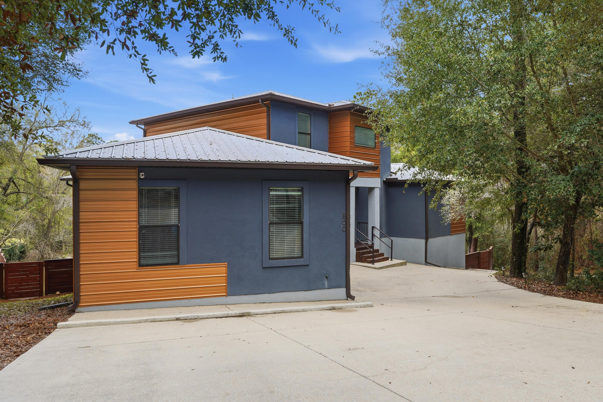 This modern mid-century masterpiece stands as a true architectural showpiece, blending striking character with effortless functionality in a highly sought-after neighborhood. Situated on a quiet street bordered by a serene creek and mature trees, the property offers a rare natural buffer of privacy complemented by peaceful lake views from the covered balcony. The main level invites you into an expansive great room that flows seamlessly to a private deck, anchored by a chef's kitchen featuring sleek concrete countertops, white shaker cabinets, and premium stainless appliances with a gas range. Retreat to the main-floor primary suite, a true sanctuary boasting a massive walk-in closet and a spa-like ensuite with a dual vanity and an oversized tiled rainfall shower. Upstairs, three generous guest bedrooms enjoy easy access to two beautifully updated bathrooms. Designed for both sophisticated living and high-end hosting, the recently remodeled walk-out lower level features durable tile floors, a dedicated home gym, a flexible fifth bedroom, and a stylish bar (which can convey). Outside, the backyard serves as a tucked-away sanctuary with a built-in firepit nestled under towering trees and a modern privacy fence. The excellence of this home extends to its "solid bones," featuring energy-efficient cement-block construction, a north/south orientation to minimize heat gain, a tankless water heater, and a durable metal roof. With over 4,400 sq. ft. of refined living space, exceptional storage--including a large locking gear room--and an unbeatable price per square foot, this home delivers a lifestyle of unparalleled comfort. Experience the pinnacle of contemporary design today; a home of this caliber is a rare find. VA Assumable loan at 2.25% Interest Rate!!! Tour today!