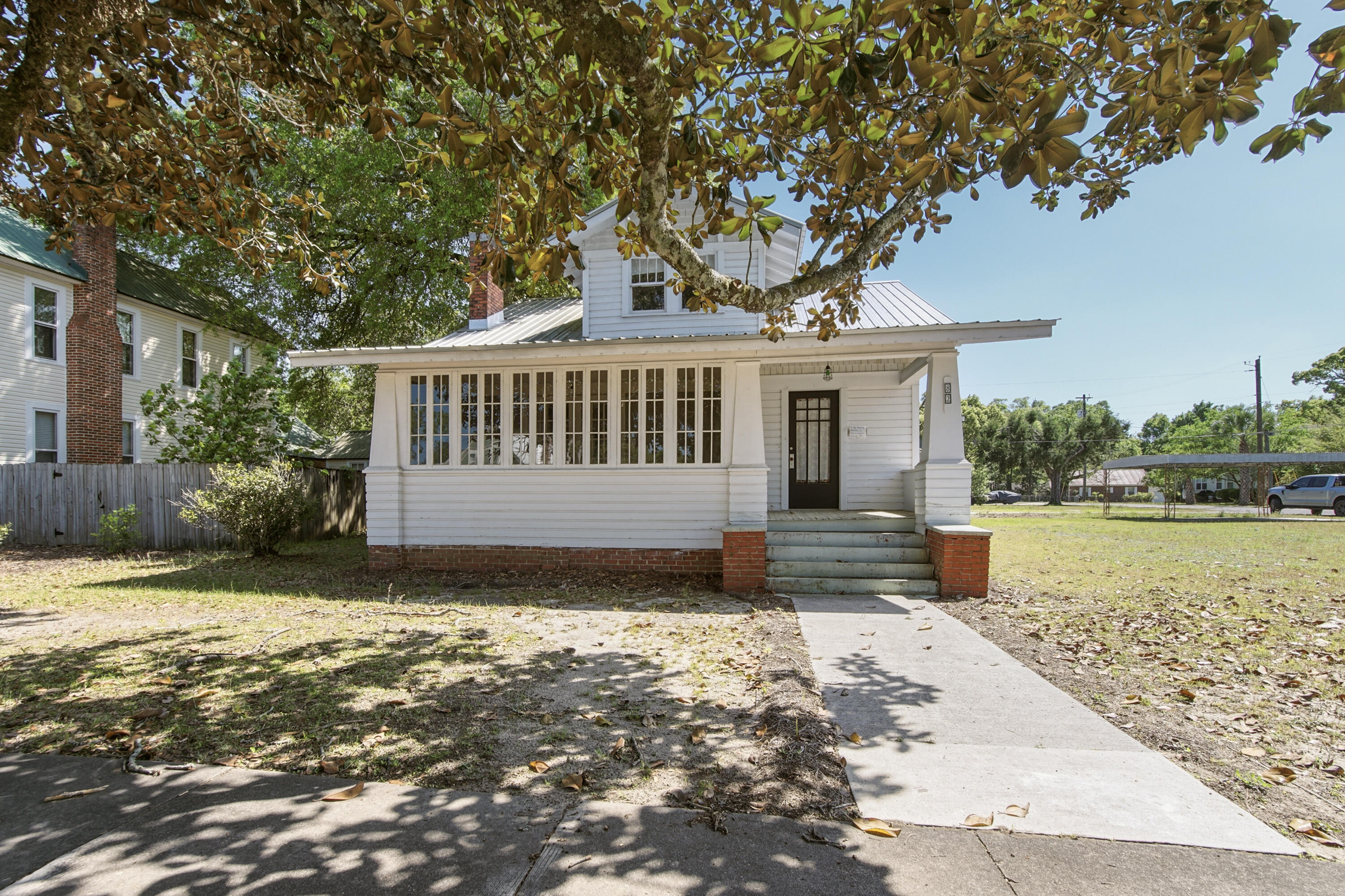 Set along E Live Oak, one of the most recognizable entry points into historic downtown DeFuniak Springs, this two-story Craftsman awaits its new owner.
Classic Craftsman columns, cedar shake accents, and a sunporch with wall to wall windows, catching all the light you'd ever want. Inside, some updates have been started, while other spaces are still waiting for the right vision to carry them forward. Out back, an older garage offers storage for now, or the chance to reimagine the space entirely. This is not a finished product, but it is a home with character, visibility and possibility. For someone who sees potential instead of projects, don't sleep on this one. The .19 acre adjacent lot may be included for total of $389,900 (lot will not be sold separately prior to home sale).