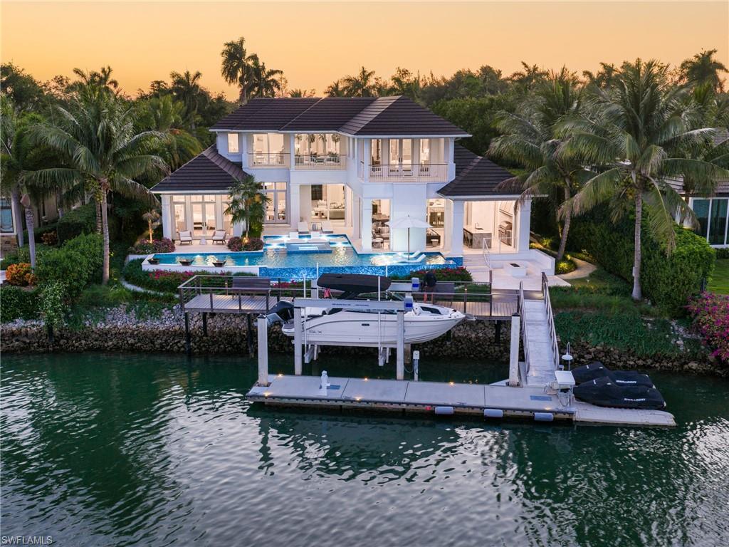 Positioned along the wide waters of Smugglers’ Bay in the prestigious community of Port Royal, this West Indies inspired estate designed by Stofft Cooney Architects, LLC represents a distinguished offering within Naples’ luxury waterfront market. Ideally located on Fort Charles Drive just moments from the exclusive Port Royal Club, one can enjoy expansive water views and a setting defined by privacy, elegance, and refined coastal living. The home offers five beautifully appointed bedroom suites and a dedicated study, with the primary suite and office thoughtfully situated on the first level for comfort and convenience. Four guest suites with an additional upstairs gathering area, provide inviting accommodations for family and guests alike. Designed with a balance of architectural sophistication and everyday livability, the residence showcases inviting interiors and a highly functional floor plan tailored to both relaxed living and entertaining. The first level features a welcoming foyer, spacious great room, large kitchen with adjoining informal dining area, formal dining room with dramatic wine display, wet bar, and a well-equipped prep kitchen discreetly positioned adjacent to the main kitchen. Multiple access points seamlessly connect the interior living spaces to the expansive outdoor environment, enhancing the home’s sublime indoor-outdoor lifestyle. The outdoor entertaining areas are equally impressive, centered around a substantial covered area featuring a fireplace, automated screens and shutters, and inviting spaces for gathering and relaxation. Adjacent to the covered entertaining space, the pool and spa with sun shelf, along with the waterside fire pit, will allow one to relax while enjoying the dramatic long-water views across the bay. A significant fixed and floating dock system with lift and observation deck further complement the property and provide an ideal setting for boating and waterfront enjoyment. With its timeless architectural design, expansive water views, Port Royal Club membership eligibility, and exceptional location, this property represents the quintessential Port Royal experience and will be further enhanced with the anticipated completion of the new Port Royal Club beach club in late 2026.