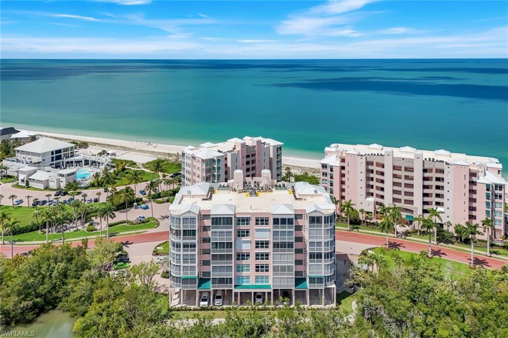 This fully reimagined coastal-modern end-unit condo in the exclusive beachfront enclave of Barefoot Beach captures the essence of elevated Southwest Florida living with sweeping bay vistas and Gulf views from the eat-in kitchen and three bedrooms! Thoughtfully redesigned with a clean, fresh, contemporary palette that feels both calming and visually striking, the interior features expansive walls of glass framing water views from nearly every angle, while the floor plan enhances privacy, openness, and connection to the outdoors. The beautifully renovated kitchen serves as both centerpiece and gathering space, appointed with quartz surfaces, sleek custom cabinetry, oversized island seating, and Gulf views that transform everyday moments into something extraordinary. Designed for effortless indoor-outdoor living, the wraparound glass-enclosed lanai, complete with storm shutters, functions as an extension of the main living spaces and can be opened to welcome coastal breezes and the sound of the waves for year-round enjoyment. The spacious primary suite continues the home’s refined aesthetic with spa-inspired finishes, generous proportions, and a custom designer closet. Each guest suite has been thoughtfully updated with its own beautifully renovated bath, offering comfort and privacy for family and guests alike. Barefoot Beach offers an elevated beachfront lifestyle with resort-style amenities, including a heated pool, fitness center, and elegant clubhouse spaces designed for relaxation and social gatherings. Buyers may inquire about incentives for membership opportunities at the private Club at Barefoot Beach, which features beachfront dining, tennis, a newly enhanced pool area, and a vibrant social atmosphere. Ideally located between Naples, Bonita Springs, and Fort Myers, residents enjoy convenient access to world-class dining, shopping, golf, entertainment, and Southwest Florida International Airport. From sunrise reflections over the bay to glowing Gulf sunsets just beyond Barefoot Beach’s sugar-sand shoreline, this exceptional residence offers a rare opportunity to experience modern waterfront living where boating, beach walks, and panoramic water views become part of everyday life.