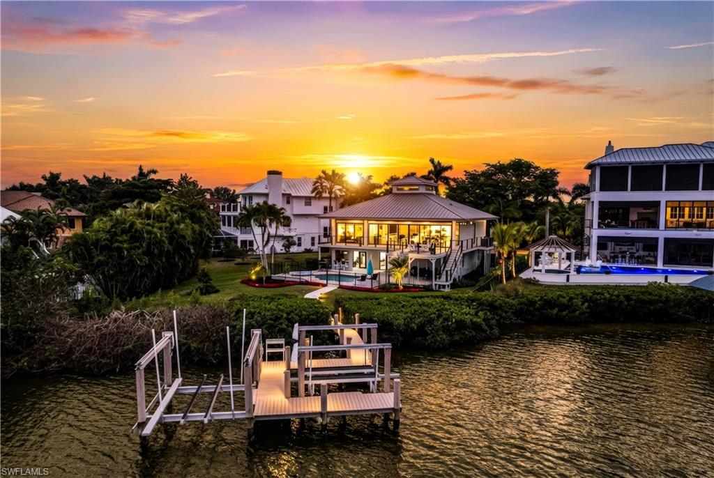 Beautiful coastal contemporary residence with breathtaking Bay views, ideally situated within the exclusive, double-gated enclave of Southport on the Bay in North Naples’ highly sought-after Barefoot Beach community. A true paradise for boaters and beach lovers alike, this exceptional property offers direct Gulf-access from your private boat dock with dual lifts, all just minutes to open water and only a short five-minute walk to the sugar-white sands of Barefoot Beach. This home features hurricane-impact windows and doors, a metal roof, a new elevator, five bedrooms, four bathrooms, and a versatile lower-level flex space. Also includes a comfortable, private guest suite well-suited for extended stays. Inside, the home showcases white oak flooring throughout and striking pecky cypress ceilings, all framed by expansive Bay views. The chef’s kitchen is impeccably appointed with Carrara marble and luxurious leathered granite countertops, white custom cabinetry, and an exceptional suite of high-end appliances, including a built-in coffee station, warming and refrigerator drawers, double dishwashers, a pot filler, and more. Outdoor living is equally impressive, featuring a wraparound deck with new decking, new cable railings, and a fire pit—an ideal setting to relax while taking in stunning water views. Below, the expansive pool deck features new marble pavers, a spacious pool and spa, covered lounging areas, and a fully equipped summer kitchen, with a partially fenced-in yard ideal for pets and additional green space beyond, all complemented by upgraded landscaping that enhances privacy. The primary suite serves as a serene retreat with private access to the wraparound deck and a spa-like bath featuring dual vanities, a soaking tub, and a glass-enclosed shower with multiple shower heads. Optional membership to the exclusive "Club at Barefoot" provides access to tennis, two restaurants, beachside food and beverage service, and more. Conveniently located near fine dining, RSW Airport, Mercato, and Waterside Shops, and just 15 miles from the renowned Fifth Avenue in Naples, this home is a true gem in the heart of Barefoot Beach.
