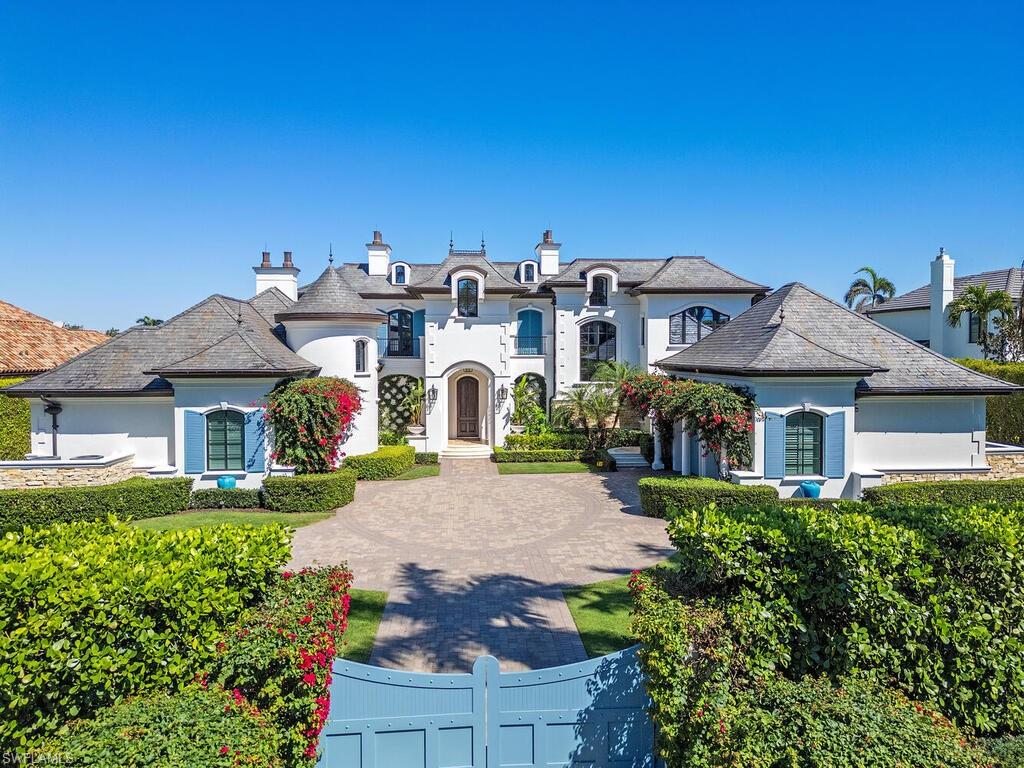 Perched on one and a quarter lots, tucked behind private gates, and framed by bright bougainvillea, this remarkable residence exudes traditional refinement with an unmatched pedigree and picturesque locale. The sophisticated 8,960 sq. ft. estate underwent a complete and comprehensive renovation throughout and offers glistening water vistas of Smuggler's Bay as a focal point from each living space that seamlessly transitions from one to the next.  In total, the main residence is comprised of four stately bedroom suites, a whimsical bunkroom with private adjacent bathroom, a handsome study outfitted in rich woods, two half bathrooms, a guest house with private ingress and egress, as well as a three-bay garage. A secondary catering kitchen provides additional convenience for entertaining. Tucked away offering the utmost in privacy, the master retreat offers sweeping vistas from both the bedroom and sun-drenched reading room, and is complete with morning bar and a truly opulent bathroom with intricate marble inlays and millwork.  Notwithstanding the copious features within, the exterior living environs are a sanctuary enveloped in lush tropical landscape and offer multiple covered terraces set for enjoyment, an outdoor kitchen, as well as a heated pool, spa, and sunshelf backdropped by tranquil water views.  Located in Naples' most esteemed community, this residence also touts an immediate Primary Port Royal Membership.