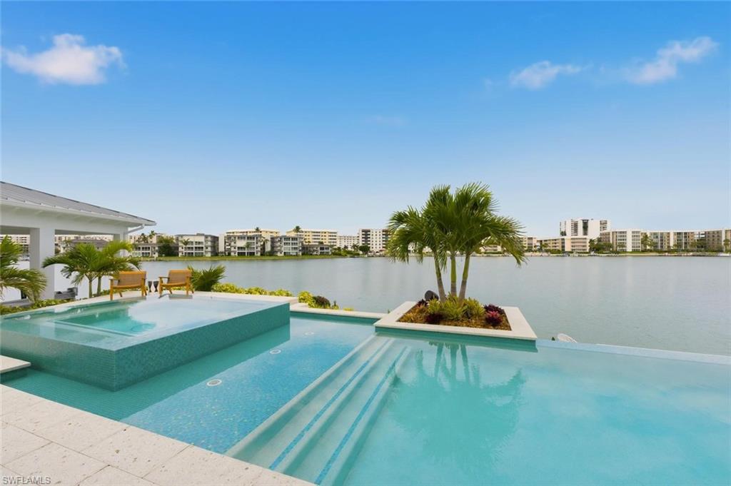 Perfectly positioned at the tip of a quiet cul-de-sac, this exceptional waterfront residence captures sweeping views of Moorings Bay from Harbour Bridge to the south to Venetian Village to the north. Fully renovated and impeccably designed, this 5 bedroom, 4 bath home defines modern luxury living. The main living area is both sophisticated and inviting, featuring a spacious sectional, custom entertainment wall, soaring vaulted ceilings, rich wood flooring, and a serene sitting area that frames the sparkling bay views. Designed to impress, the chef’s kitchen showcases top-tier finishes, including an expansive island with seating for seven, an oversized refrigerator, wine cooler, and sleek white cabinetry. The open-concept layout flows effortlessly into the elegant dining area, highlighted by statement lighting and seating for eight—perfect for entertaining. The primary suite is a true retreat, offering a king-sized bed and a wall of windows overlooking the water. The spa-inspired primary bath features dual vanities, a soaking tub, an oversized walk-in shower, and a custom walk-in closet. Three beautifully appointed guest bedrooms, each with queen-sized beds, provide comfort and privacy for family and guests. A fifth bedroom currently serves as a stylish den with dual workspaces and a cozy seating area, with the option to convert it into a bedroom upon request. Just outside is your private waterfront oasis, boasting 170 feet of frontage, a resort-style pool, boathouse, gas fireplace, and lush tropical landscaping with swaying palms—an ideal setting for relaxation or entertaining. Residents also enjoy eligibility for membership to the exclusive Moorings Beach Park. This remarkable home offers a rare opportunity to experience the very best of Naples waterfront living. Live exceptionally in The Moorings.