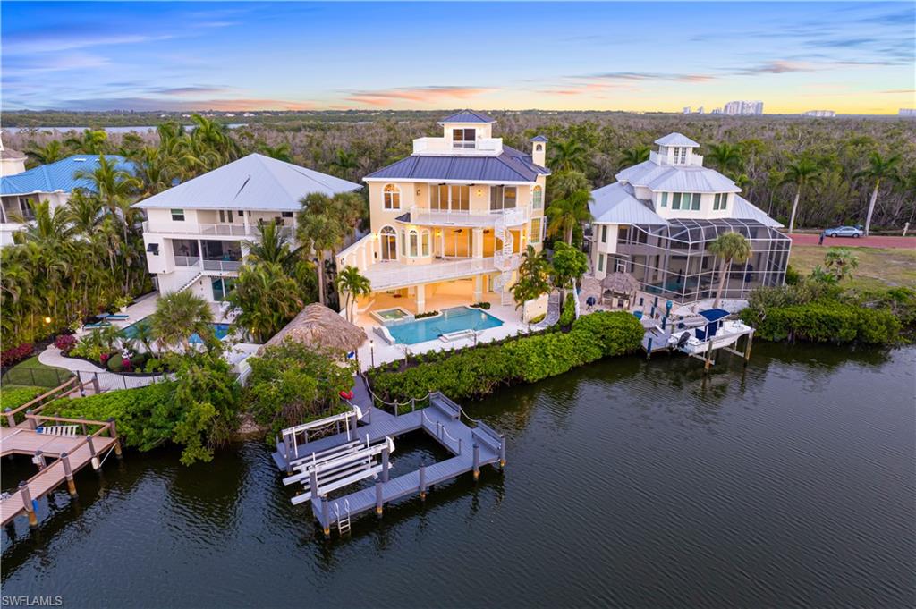 One or more photo(s) has been virtually staged, AI generated or rendered.  4% FINANCING OFFERED BY SELLER!* Spectacular coastal living in Barefoot Beach’s premier gated enclave. Experience the epitome of coastal luxury at this extraordinary residence, nestled in the exclusive double-gated Bayfront neighborhood of Barefoot Beach. With panoramic Bay views, direct boating access to the Gulf, and deeded beach entry just steps away, 235 Bayfront offers a lifestyle defined by elegance, comfort, and coastal sophistication. The home showcases extensive upgrades, including a newly installed 48” custom flood barrier system (approx. $30,000), a new elevator, impact doors/windows, electric shutters, whole-house water purification system, generator with 500-gallon buried propane tank, six HVAC units, newer water heater, Moen smart water shutoff, and central vacuum system. This 5-bedroom + den, 5.5-bath, 4-story estate features a heated saltwater pool and spa with new equipment, outdoor shower, and tiki hut with a summer kitchen and bar seating—perfect for entertaining or relaxing in style. A private boat dock with new motors and controls allows for a 10-minute ride to the Gulf, and the beach is only a 5-minute walk away. Interior highlights include a refinished first floor with new flooring, woodwork, and doors, two full laundry rooms, plantation shutters and oversized windows throughout, a 2-story great room with soaring ceilings, and an expansive primary suite with breakfast bar. The top-level “cloud room” with a custom bar offers the most breathtaking Bay views, complemented by balconies on every level. Located in a quiet, gated enclave where homes line only one side of the street—offering unmatched privacy and unobstructed water views. Optional membership to the exclusive "Club at Barefoot" provides access to tennis, two restaurants, beachside food and beverage service, and more. Conveniently located near fine dining, RSW Airport, Mercato, and Waterside Shops, and just 15 miles from the renowned Fifth Avenue in Naples, this home is a true gem in the heart of Bayfront Gardens in Barefoot Beach. Elegant, functional, and move-in ready—this is elevated waterfront living at its finest.