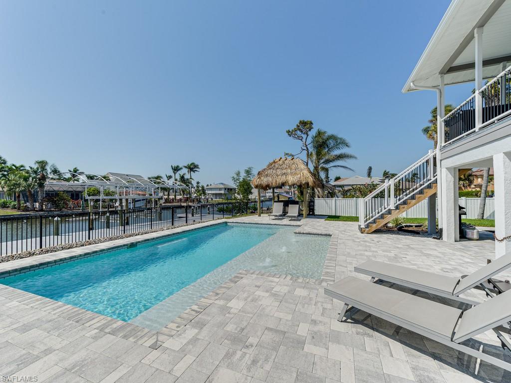 H9057. Gulf access gem, within walking distance to Barefoot Beach. The backyard entertaining area is 2nd to none.  This wide canal property has been used as a primary residence and rented AirBnB for $16-20,000/month by prior owner. Pool and tiki hut overlooking the canal have all been redone and make this the perfect entertaining paradise. The seawall is in excellent condition.  Additionally, there is a 10,000-pound boat lift, with new motors and new jet ski lift.  Outside entertaining area is impeccable.  The 2nd floor features two phenomenal bedrooms/two bathrooms with an open floor plan and custom finishes.
The first floor has been remediated & taken down to the studs The re-configuration possibilities are endless.  There are also approved plans for 2nd floor expansion. Property can be restored to original configuration (2 bedroom, 1 bath downstairs with kitchen) or totally upgraded to 2 car garage with 3 bedroom/3 bath upstairs and crow’s nest above roof to watch sunsets.  Air conditioning, electric & plumbing have all been replaced.  Kinetico water softening system with reverse osmosis has been added. Area has new infrastructure recently installed by county.
