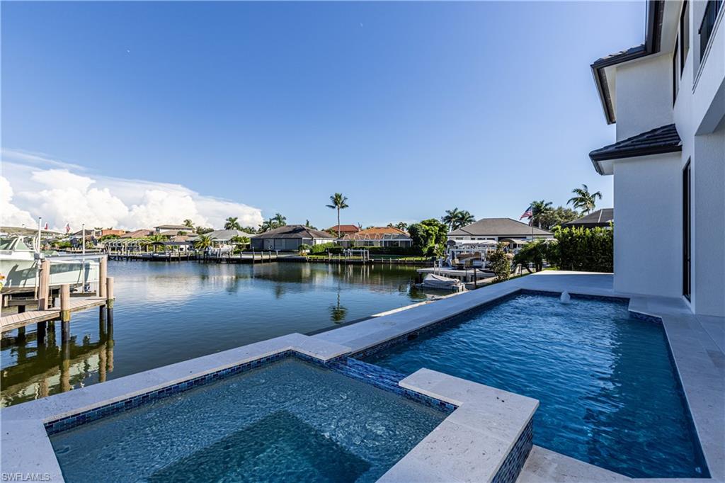 This brand new coastal contemporary Marco Island custom home is move-in ready and designed to maximize water views, natural light, and luxury living. Offering over 4,000 square feet under air, it features five bedrooms, four and a half bathrooms, a family loft, and multiple indoor and outdoor living spaces perfect for entertaining and relaxing. Step through the grand two-story foyer into the open-concept great room, both soaring 23 feet high and drawing your eye through 41 feet of sliding glass doors to breathtaking water views. The gourmet kitchen is a chef’s dream with premium Thermador appliances, a gas range, and a hidden walk-in pantry. High-end quartz countertops and plank-style flooring run throughout the home. The first floor includes a large family room, an additional living area, a master suite with a spa-inspired bath, and a second bedroom that could serve as a private office. Upstairs, the loft overlooks the great room and opens to a large covered balcony facing the water. The second floor also includes two bedrooms, two bathrooms, and a bunkroom (5th bedroom). Outdoors, the home showcases 80 feet of waterfront on a long, uninterrupted 1,400-foot stretch of canal, providing expansive water views. The backyard includes a swimming pool with sundeck and spa, and a fully equipped outdoor kitchen. Additional highlights include a 500-gallon underground propane tank pre-wired for a generator, southeastern exposure for abundant sunlight, and a central Marco Island location within walking distance to the YMCA and near the island’s elementary and middle schools. Priced under $1,000 per square foot as a 2025 construction, this home offers exceptional waterfront luxury and unmatched value among new homes.