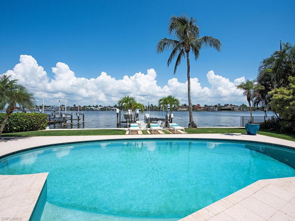 Perched on one third of an acre along the dynamic Naples Bay with 82 ft. of water frontage, this Bermuda-style residence personifies Bespoke Old-Florida charm and would make a fantastic intermediary residence while plans are solidified to construct the bayfront oasis of your exact specifications. The all one-level main residence and guest house are located down a private lane and offer three bedrooms plus open study area, as well as three full bathrooms.  A myriad of architectural details are found throughout, providing warmth and style, such as wood-beam exposed ceilings in the formal living area, two wood burning fireplaces wrapped in stone, a family room with floors coated in original terrazzo, as well as both striking and modern kitchen / bathrooms.  Meeting the rolling lawns ledge, a walkway, and dock with two boat lifts, allows residents quick access to the deepwater yacht basin that is their backyard. Located in the heart of Aqualane Shores, the surrounding neighborhood is known for it's stunningly palm-tree lined streets and avenues, being home to numerous deep waterways, and the array of  and local establishments for dining and shopping - all the while located a short stroll to Naples' sugar sand beaches. Being sold As-Is for lot value only.