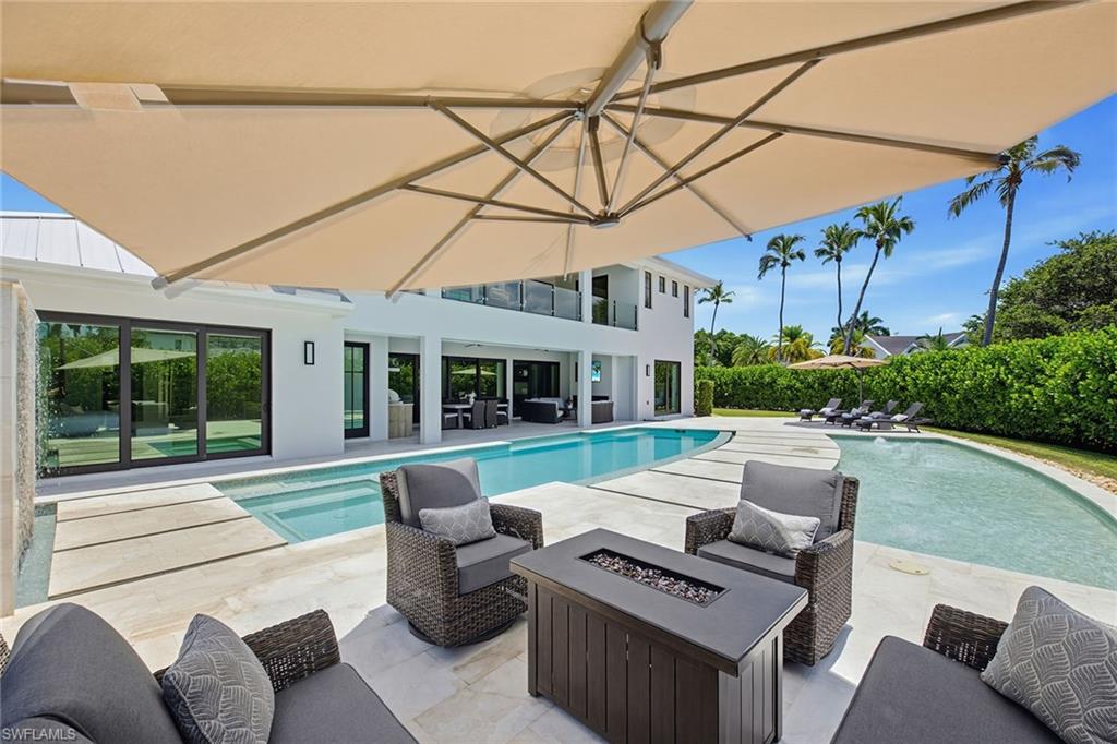 Completed in 2024 by Gulfstream Homes and offered beautifully furnished by Clive Daniel, this exceptional Coquina Sands residence captures the essence of the Naples coastal lifestyle. Positioned on an oversized, south-facing corner lot, the property is enveloped by a lush privacy hedge that creates a secluded setting just moments from the beach, Lowdermilk Park and Fifth Avenue South. A private driveway and three-car garage with access from Banyan Circle provide added convenience and functionality, a rare offering in this coveted neighborhood. Designed for effortless indoor-outdoor living, the expansive backyard is one of the property's defining features. Rarely found, the oversized outdoor space offers room to entertain, relax and enjoy the Florida sunshine with a massive resort-style pool featuring a sun shelf, spa, water features and an expansive pool deck with multiple gathering areas surrounded by tropical landscaping. The spacious covered lanai extends the living experience with a fireplace, summer kitchen and electric screens and storm shutters, creating a comfortable setting for year-round enjoyment. Inside, soaring tongue-and-groove ceilings and walls of glass fill the great room with natural light while seamlessly connecting to the outdoor living spaces. The open-concept kitchen is thoughtfully designed with custom solid wood cabinetry, quartz countertops, an oversized Sub-Zero refrigerator and freezer, induction cooktop that is plumbed for gas, generous storage and a dedicated beverage and wine bar. The main-level primary suite is complemented by a private study, and guest suite, while the second level offers a lounge with wet bar, beverage refrigerator, three guest suites with large balcony access and a second laundry area. A private elevator, custom closet systems throughout, electric shades in private spaces, whole-home generator with a 1,000-gallon propane tank and location within the desirable X flood zone complete this exceptional coastal residence.