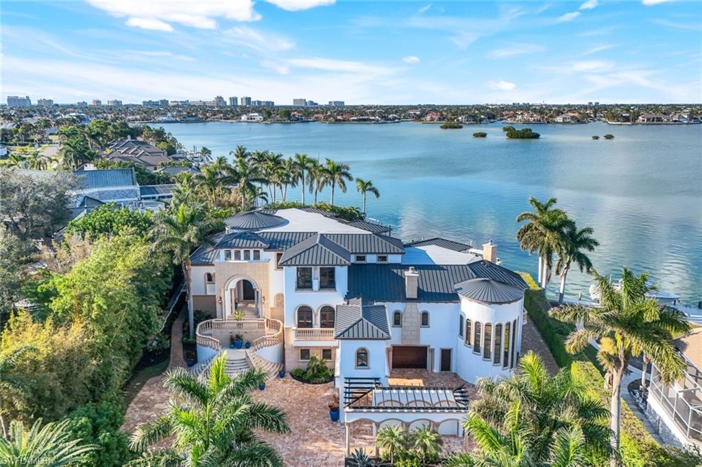 Welcome to an extraordinary estate of grandeur and refinement on Marco Island, where 9,481 SF of sophisticated living space meets an impressive total of 15,072 SF, elevated 18 feet above sea level for ultimate peace of mind. This rare .87-acre gated estate offers privacy, lush landscaping, and stunning wide sunset views of Roberts Bay, complemented by deep-water direct access with a slip for up to a 47-ft boat on a 36K LB lift with additional jet ski/flat boat platforms. The ground-level, climate-controlled garage spans 4,075 SF and accommodates 14 vehicles with custom epoxy flooring, 2 lifts, and room for more. Designed for the automotive enthusiast, it features a full-size fitness center, billiards room, tackle room, gun-safe room, workbench, and a lounge area making for an unparalleled "man cave." Enveloping you in an atmosphere of refined grand scale elegance discover inside, the hewn doors, barrel-vaulted, coffered, and domed ceilings, soaring archways, Corinthian columns and meticulous painted finishes, enhanced by Control4 automation throughout the home, epitomizing ultimate luxury. A 2-story great room, with soaring cathedral windows, showcases wrought iron railings, marble floors, and multiple sparkling chandeliers. An expansive chef's kitchen boasts stunning countertops, a massive island, and top-tier appliances with a sun filled breakfast room, full butler's pantry and formal dining room nearby. Dual his-and-her studies offer a harmonious blend of productivity and privacy, for focused work and personal reflection.The luxurious primary suite includes a private patio, steam shower, spa-like bath, and walk-in closets that double as a safe room. Upstairs, a bridge connects 3 beautifully appointed private ensuites, one jack and jill, with a massage room. Nearby find a home theater with seating for 11. Two elevators provide access with one dedicated exclusively to the kitchen and service areas. The rear outdoor space cascades elegantly toward the waterfront, featuring a serene reflecting pool with a tranquil water feature and a fully equipped outdoor kitchen that includes a pizza oven, built-in grill, refrigerators, and ice maker, all perfectly designed for luxurious outdoor entertaining, with music piped through the interior and exterior refining your experience. Terraced landscaping, enhanced by sophisticated outdoor lighting, guides you to the sculpted vanishing-edge pool and waterfall spa, creating breathtaking ambiance. Drive seamlessly from your car to your boat, enjoying an effortless luxury lifestyle. This extraordinary property is a masterpiece of thoughtful design, unparalleled privacy, and modern convenience, crafted on a grand scale to exceed the expectations of the most discerning buyer.