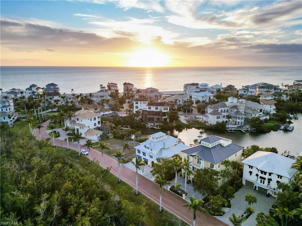 Exquisitely renovated home with breathtaking bay views nestled in the exclusive, double-gated Bayfront Gardens within the prestigious Barefoot Beach community of North Naples. A true sanctuary for boating enthusiasts and beach lovers alike, this property provides direct Gulf access within minutes (no bridges) and is less than a 5-minute walk (0.2 miles) to the deeded resident only beach access at Barefoot Beach. Designed for the ultimate waterfront lifestyle, the residence boasts a brand-new boat dock and lift, perfect for quick access to the Gulf. Built like a fortress, this residence boasts concrete block construction on the bottom two floors, hurricane impact windows and doors, and a metal roof. Other features include a Generac generator, 800 gal buried propane tank, and an On-Demand hot water heater. Inside, you’ll find 4 spacious bedrooms, a den with a wet bar, 4 bathrooms, a versatile ground-floor flex space, and a 3-car garage. The interior has been thoughtfully renovated in a gorgeous coastal contemporary style. Step outside to discover a resort-style outdoor oasis, perfect for entertaining or relaxing. The expansive lanai offers captivating bay views, a pool and spa, an outdoor shower, and a tiki hut with a built-in grill. The chef’s kitchen is a culinary dream, featuring crisp white cabinetry, granite countertops, glass-tiled backsplash, and top-tier appliances, including a Wolf microwave, double oven, gas range, Sub-Zero refrigerator/freezer, and a 136-bottle wine fridge. The spacious primary suite is a true retreat, offering sweeping bay views and a spa-like bathroom complete with dual vanities, a large glass-enclosed shower with multiple shower heads, and a separate soaking tub. On the top floor, a cloud room awaits—a serene sanctuary perfect for unwinding and enjoying the breathtaking vistas. The wraparound balcony extends the experience, providing a tranquil space to soak in the stunning water views. Bayfront Drive homes are uniquely positioned on one side of the street, offering unparalleled privacy and unobstructed views of the bay. Conveniently located near fine dining, RSW Airport, Mercato, and Waterside Shops, and just 15 miles from the renowned Fifth Avenue in Naples, this home is a true gem in the heart of Bayfront Gardens in Barefoot Beach.