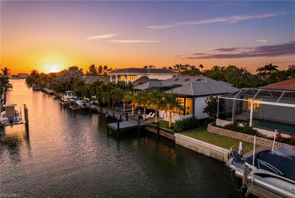 Discover an exquisite waterfront sanctuary at 1506 Jewel Box Avenue, perfectly positioned on one of Royal Harbor’s widest canals. This exceptional property offers an impressive 130 feet of total water frontage with two private docks and bridge-free access to Naples Bay and the Gulf waters—ideal for avid boaters seeking seamless adventures on the water.  Completely transformed into a sophisticated modern masterpiece, this 2,777-square-foot residence has never flooded and sits at 10.25 feet elevation.  Its design thoughtfully blends organic materials with cutting-edge smart technology, and every detail has been meticulously curated for beauty, functionality, and enduring value. The open living spaces feature soft hardwood floors, recessed LED lighting, upgraded interior doors, designer fixtures, and striking architectural ceiling beams.
A desirable split floor plan centers around an expansive, panoramic screened lanai with a resort-style pool, promoting effortless transitions between formal and casual living, indoor elegance, and outdoor relaxation. The gourmet kitchen is a chef’s dream, equipped with premium brushed black Samsung appliances, natural stone countertops, soft-close wood cabinetry, a generous breakfast bar, convenient recessed charging station, and subtle under-cabinet toe-kick lighting.  

The luxurious primary suite serves as a private waterfront retreat, complete with serene canal views, dual walk-in closets, and a spa-inspired bathroom featuring a freestanding soaking tub, separate rain shower, dual vanities with backlit LED mirrors, and a state of the art smart toilet.
On the opposite wing, two additional bright and spacious bedrooms offer ample closet space for ultimate privacy. A versatile fourth bedroom with double French doors doubles perfectly as a home office, den, or meditation room.  The multifunctional laundry room elevates everyday convenience with custom cabinetry, a utility sink, built-in drying racks, and direct access to the climate-controlled two-car garage.

Outdoor living is equally impressive, designed for year-round enjoyment. The pool area boasts a sun shelf, integrated spa, elevated swing seating, custom dynamic lighting, and built-in fountains. A third full bathroom is conveniently tucked under the covered lounge with a built-in gas fireplace. Landscape lighting creates magical ambiance throughout the entry garden, rear deck, and docks. What truly distinguishes this home is its unparalleled boating lifestyle. The rear features an expansive Trex deck with outdoor shower, sun lounge area, swim platform and a 65-foot dock. Across the street, an additional 65-foot dock includes a 30,000-pound boat lift and protective canopy, plus four bonus parking spaces. All this awaits on a peaceful, quiet street in the prestigious Royal Harbor neighborhood—minutes from downtown Naples’ world-class dining, shopping on 5th Avenue South, and pristine Gulf beaches. Experience refined coastal living at its finest!