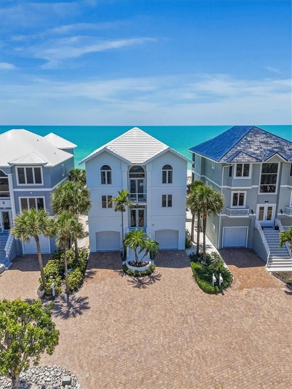 Direct Gulf-front. Direct beach access. Inside the gates of The Cottages at Barefoot — one of Southwest Florida's most private coastal addresses, where fifteen residences share a single stretch of white sand. This is one of them. From its westward orientation, the horizon belongs to it.
Three stories of light-filled coastal living rise above the beach, served by a private in-residence elevator. The main living level opens to the Gulf through walls of floor-to-ceiling glass that pull the ocean into the room. A fireplace anchors the great room. Tray ceilings, custom built-in cabinetry, and a wet bar with mirrored backsplash, glass-front display, and integrated wine rack carry the level of finish through the principal entertaining spaces.
Bay windows with built-in window seats frame the water from multiple vantage points. Arched display niches and custom architectural detail elevate the formal dining room. A gourmet kitchen delivers stainless appliances, white cabinetry with decorative hardware, an integrated desk station, and recessed lighting throughout. Beyond the main level, a beamed-ceiling solarium opens to full ocean exposure and houses an in-room spa — the kind of private retreat that defines this category of home.
The primary suite delivers marble countertops, dual undermount sinks, and a glass-enclosed rainfall shower. A dedicated home office is finished with extensive custom built-ins. Four bedrooms in total, plus a den, family room, dedicated laundry, and screened lanai. 2,962 square feet of living area; 4,156 total under roof.
Construction is concrete block with stucco exterior and a tile roof — built for life on the Gulf. Hurricane shutters. Double-hung windows. Two-single car attached garage opens onto a paver drive framed by mature palms. The paver patio walks directly onto the sand.
Optional membership is available to The Club at Barefoot Beach— resort-style pool, oceanfront dining, beachfront fire pit lounge, and tennis. The Cottages at Barefoot is a fifteen-unit condominium community with architectural standards, sidewalks, and streetlights. Pets welcomed with approval. Barefoot Beach is guard-gated, low-density, and bordered to the south by a state preserve. Direct Gulf-front opportunities inside this gate are rare.