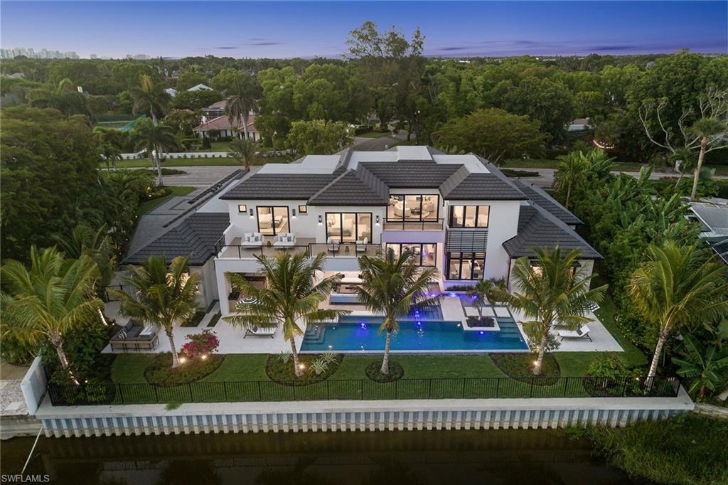 Vista Lago. On a prized southern-facing waterfront estate lot, this newly constructed, custom-curated home offers unmatched luxury, two blocks from Gulf beaches and the anticipated Naples Four Seasons Resort, capturing sweeping panoramic views across tranquil waters to the Fazio-designed championship golf course. This exquisite custom masterpiece is a triumph of luxury and architectural artistry. Encompassing 6,909 square feet of under-air living space, with a total build area of 11,742 square feet, the open-concept floor plan flows effortlessly between indoor and outdoor living, creating an ambiance of casual elegance and grandeur. The ultra-luxury interior selections for the home were expertly curated by the award-winning Freestyle Interiors, blending timeless design with today’s sophisticated modern trends. Six spacious bedrooms with en suites, a private study, fitness room, and an open loft provide refined comfort and versatile functions. The gourmet kitchen is a culinary dream, with exquisite custom cabinets and Cristallo hand-fluted counters, a separate fully equipped chef’s kitchen, custom coffee bar, and a sophisticated wine station highlights the Italian marble wall and island. Walls of glass reveal serene vistas from the expansive kitchen, living and dining spaces, all oriented toward the outdoor sanctuary. The waterfront resort-style pool and spa are surrounded by dining and lounge areas, along with a fully appointed outdoor kitchen, ideal for unforgettable entertaining. For the car enthusiast, the four-car air-conditioned garage is thoughtfully designed with capacity to accommodate up to eight vehicles with lifts. Penned by BECK Architects and expertly built by renowned Parker Hudson Homes, this is more than a home, it is an extraordinary lifestyle statement, where luxury meets legacy. Minutes to downtown Naples and a short distance to the beach. This is the epitome of the Naples lifestyle.