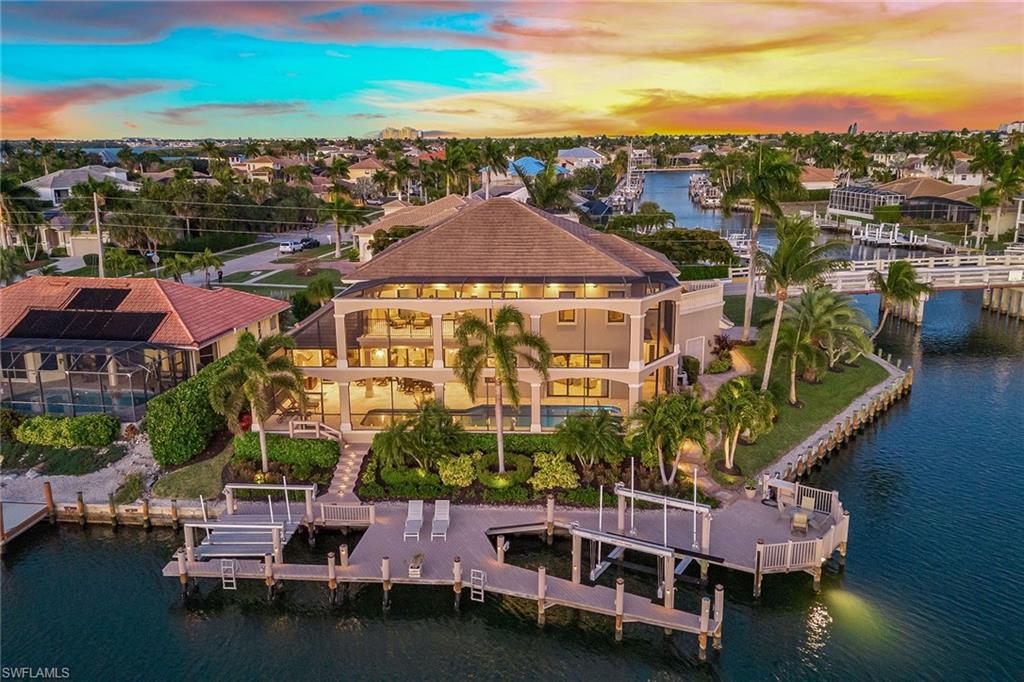 Welcome to this stunning custom waterfront estate, offering six bedrooms plus a study, 6.5 baths and breathtaking bayfront sunsets with quick gulf access. Ideally just blocks from the beach and close to Marco Island's top attractions, this elegant residence seamlessly blends luxury, comfort and impeccable design. Step through stately double doors into a grand entryway featuring a solid-wood staircase, private elevator, soaring ceilings with crown molding, designer lighting and marble floors. The living room's beam ceiling is a showpiece, complemented by a built-in entertainment center and dry bar. The gourmet kitchen is a chef's dream, boasting floor-to-ceiling ivory and walnut cabinetry with underlighting, granite countertops, and a massive 12-by-6-foot island with a sink and under-counter ice maker. Premium Thermador appliances include a wall oven, two dishwashers, and a wine tower refrigerator. A pass-through connects the kitchen to the formal dining room, enhancing the home's flow for seamless entertaining. The breakfast area enjoys scenic water views, while a pass-through window to the outdoors makes alfresco dining effortless. This exceptional home features owner's suites on both levels, a large loft with a wet bar, a den and two balconies, one open air and another off the main suite that can be shuttered for privacy. The upstairs common room features a queen-size sofa bed, adding flexibility for guests. Outside, a two-story screened colonnade encloses expansive covered and uncovered living areas, a cedar ceiling, a heated pool with spa and sun shelf, and a built-in gas grill with hood. The pool bath features a walk-in shower with a frameless glass enclosure and floor-to-ceiling tile, providing convenience and elegance for poolside living. The private composite dock is fully equipped with a 20,000-pound boat lift, platform lift and sundeck. Additional features include a 2018 cement tile roof, impact glass, tray ceilings, custom closets, home automation, surround sound, video security, central vacuum, a jetted tub and a two-car garage with an epoxy floor and built-in cabinets. Enjoy the best of Marco Island living, from boating and award-winning beaches to boutique shopping, golf, tennis, pickleball, fine dining, cultural attractions and a nearby executive airport. This extraordinary home is the island retreat you've been waiting for.