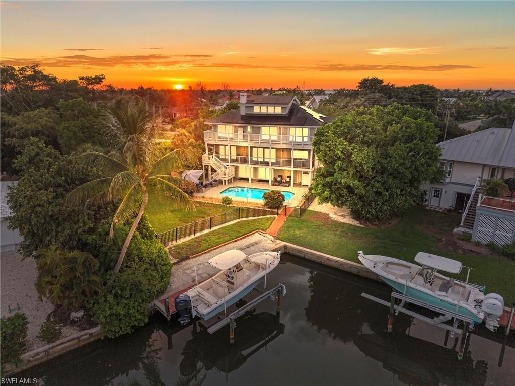Welcome to 1048 Kings Crown Drive, a remarkable waterfront residence designed by renowned Sanibel architect Joe St. Cyr. Located in the private beach-access community of Shell Harbor on Sanibel’s coveted East End, this elevated 5-bed, 4-bath home offers an exceptional blend of architectural pedigree, luxury finishes, and waterfront living. Perfectly positioned for convenient on-and-off island access while maintaining privacy and tranquility, the home showcases St. Cyr’s signature appreciation for natural light, island breezes, and seamless indoor-outdoor living.
Over the past few years, every aspect of the interior has been updated, blending timeless island architecture with sophisticated modern luxury. Meticulous attention to detail is evident —from dramatic shiplap ceilings and designer lighting to exquisite finishes and curated tile selections. The result is a stunning coastal retreat that feels both refined & welcoming.

At the heart of the home, on the elevated main living level, a spectacular chef’s kitchen features a striking oversized mitered-edge island with seating for six. Culinary enthusiasts will appreciate the professional dual-fuel Thermador six-burner range with griddle, an expansive main oven, and warming oven. Additional highlights include a full-height integrated wine refrigerator, built-in Miele coffee station, & abundant floor-to-ceiling custom cabinetry. Telescoping windows and doors create a seamless connection between indoor and outdoor living, while a pass-through counter opens to an outdoor breakfast and cocktail bar, making entertaining effortless. Expansive windows frame tranquil canal views, where dolphins and manatees are frequent visitors and can often be spotted from the kitchen, living areas, and primary suite. This level also features a private guest suite with a beautifully appointed ensuite bath, a two-sided fireplace anchoring an intimate sitting area, and an oversized great room designed for effortless entertaining.

Occupying a privileged position on the third living level, the luxurious primary suite offers tranquil canal views, a spacious walk-in closet, and a spa-inspired bath. Designer finishes include a freestanding soaking tub, oversized walk-in shower with multiple shower heads, a stunning Palecek chandelier, backlit vanity mirrors, and a beautifully crafted custom oak vanity.
The third level also features three generous, light-filled guest bedrooms, all with private balcony access, two additional designer baths, and a convenient laundry area. The fourth-floor bonus room is wrapped in windows showcasing sweeping island views. Currently utilized as a media and lounge space, this flexible area could easily serve as a home office.
Set on a fenced double lot, the property features an oversized swimming pool, private dock, and 10,000-pound lift. Residents of Shell Harbor enjoy private gated beach access just a short bike ride away. This exceptional residence offers the very best in Sanibel Living!