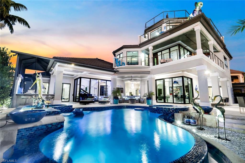 Welcome to 1518 Hermitage Ln, a breathtaking statement of modern luxury located within the prestigious, gated Hermitage community of Cape Coral with southern exposure and spectacular water views, this residence embodies the pinnacle of Florida living. From the moment you enter, you are greeted by soaring sophistication—stunning living and formal dining spaces anchored by a dramatic 150-bottle wine cellar wall, perfectly framing endless water vistas.  Designed for both refined living and grand entertaining, the gourmet kitchen is a showpiece featuring dual islands, cooktop, double ovens, exotic quartz countertops, contemporary wood cabinetry, under-cabinet lighting, and designer fixtures throughout. A dedicated coffee bar with mini fridge adds convenience and style. The adjacent game and entertaining area boasts a full bar, fireplace, and pool table, creating a seamless flow for hosting.  The ground-floor primary suite is a private retreat with modern accent walls, elevated window coverings, and recessed lighting. The spa-inspired primary bath is truly unforgettable—highlighted by an enormous fully enclosed glass shower with multiple shower heads, dual vanities, a freestanding soaking tub, makeup station, and mini fridge. This level encompasses 2 more En-Suites finished with impeccable detail. Take the staircase or pneumatic elevator to the second level, where there is a 3rd guest en-suites with 90 degree slider with open balcony.  Additional interior spaces include a private gym, theater room, and home office/den.  Outdoors, this residence defines luxury Florida living. Enjoy three balcony levels, a spiral staircase leading to the fourth-level cupola, and a resort-style pool complete with built-in spa, fire bowls, fountains, and a fully equipped outdoor kitchen. Boaters will appreciate the expansive composite captain’s walk dock with two boat lifts, including a 28,000-lb lift (2021) with canopy for sun protection and a 10,000-lb lift (2024). Laundry room is equipped with a laundry tub and DOGGIE WASH.  Car enthusiasts will appreciate the Oversized four-car garage over 1,100 sq ft, impeccably finished with exquisite epoxy floors and elegant wainscoting, elevating even the garage spaces to luxury standards. This home is as functional as it is beautiful, featuring a new tile roof (2021), four A/C units replaced in 2021 (including garage mini-splits), new appliances (2022), two hot water heaters replaced in 2023, an Insta-hot system (2022), and new pool pumps (2022 & 2024). Complete hurricane-impact windows and doors throughout, with no water intrusion during recent storms, provide exceptional peace of mind.  An unparalleled offering where cutting-edge design and waterfront elegance converge.