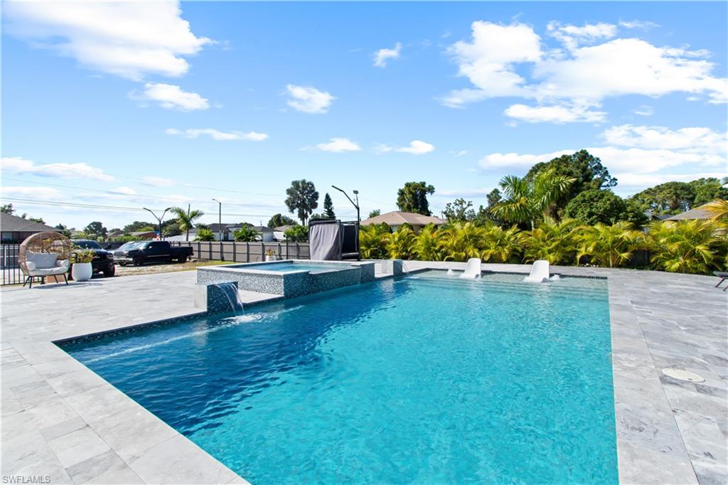 Welcome to one of the most extraordinary homes in Lehigh Acres, proudly set on a rare HALF-ACRE LOT—a feature almost impossible to find in this area. This custom-built modern residence is more than a home… it’s a private resort, crafted for those who want beauty, privacy, and luxury wrapped into one unforgettable property.
Inside, you’ll find soaring tray ceilings, oversized marble-inspired porcelain floors, and an airy open floorplan that flows seamlessly from the living room to the chef’s kitchen. The kitchen impresses with quartz countertops, a massive island, premium cabinetry, stainless steel appliances, and elegant pendant lighting. The spacious primary suite offers a true retreat with its designer tray ceiling, luxury tile, freestanding tub, walk-in shower, and floor-to-ceiling custom tile.

The real showstopper is the resort-caliber backyard—one of the finest outdoor living spaces in all of SWFL. this property was transformed with high-end upgrades, including:
    •    Custom 18’ x 35’ pool with oversized sun shelf
    •    12’ x 12’ infinity-edge spa with dual waterfalls
    •    3,000 sq. ft. of marble pool deck for entertaining
    •    Full color-changing outdoor lighting system
    •    Dedicated custom aluminum BBQ pergola
    •    Prestige Italian luxury stone table under the main pergola
    •    Artificial living wall for style & fresh air
    •    Turf areas for gatherings & low maintenance
    •    Custom bar, fridge, rustic backsplash & epoxy details
    •    Signature landscaping with Christmas palms + concrete curbing
    •    Fully fenced property with integrated added rear lot

With over 21,000+ sq ft of usable land, you’ll enjoy unmatched privacy and space for RVs, boats, toys, expansions.
This is more than a property… it’s a lifestyle. A home built to impress, entertain, and elevate everyday living. Homes like this simply do not come around often—especially not with half an acre, a resort-style outdoor oasis, and this level of detail.
