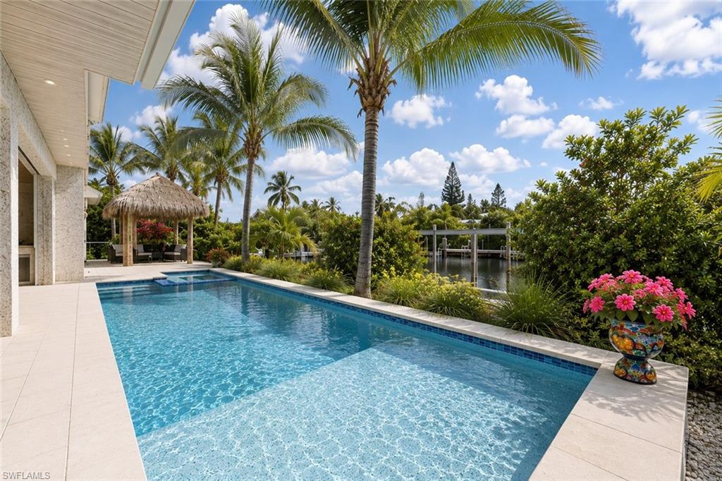 Pristine, and move-in ready, beautifully decorated custom waterfront residence, known as “The Seashell House,” ideally positioned on a quiet canal in Royal Harbor with quick no-bridge access to Naples Bay and the Gulf of Mexico. Wrapped in gorgeous Coquina shell stucco, the home captures the ultimate coastal feel of living on the water just moments from the beach, combining timeless character with relaxed luxury waterfront living. Thoughtfully designed for both everyday comfort and entertaining, this exceptional home offers an incredibly functional floor plan with the primary suite, two guest en-suites, and a private office/den all located on the first floor. The second level lives like its own private guest retreat, featuring an exquisite VIP suite, spacious loft-style living and dining area, sweeping waterfront veranda, and a fully equipped exercise studio with sauna and shower that can also function as a fifth bedroom. Both first and second-floor laundry rooms add convenience, along with gas-heated appliances throughout the home. Designed to embrace the Naples waterfront lifestyle, the outdoor living area is exceptional, complete with a covered dining and lounge space, built-in grill and refrigerator, automated roll-down screens, and a gas-heated saltwater pool and spa. The expansive patio and charming tiki hut create the perfect setting for entertaining family and friends year-round. Boating enthusiasts will appreciate the newer seawall, 65-foot IPE dock, and 10,000-pound boat lift, all completed in 2015, allowing for effortless boating access to the Gulf with no bridges. The gorgeous Coquina shell stucco exterior adds warmth, character, and timeless coastal charm, while a whole-house generator with a 750-gallon tank provides additional peace of mind. Being offered furnished, including a Tesla charging station, this meticulously maintained residence is truly move-in ready for the next owner to immediately begin enjoying the Royal Harbor lifestyle. First time available on the market and ideally located within walking distance to Downtown 5th Avenue South, world-class dining and shopping, and Naples’ famous white sandy beaches. One or more photo(s) has been virtually staged, AI generated or rendered.